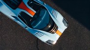 Light blue sports car with an orange racing stripe down the center, viewed from above on asphalt.