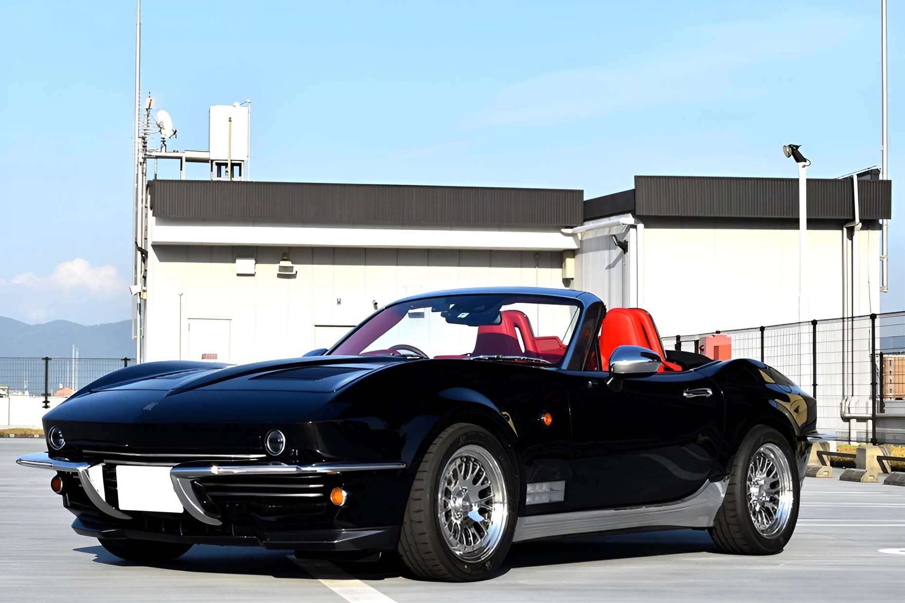 Black convertible sports car with red leather seats parked on rooftop under clear sky.