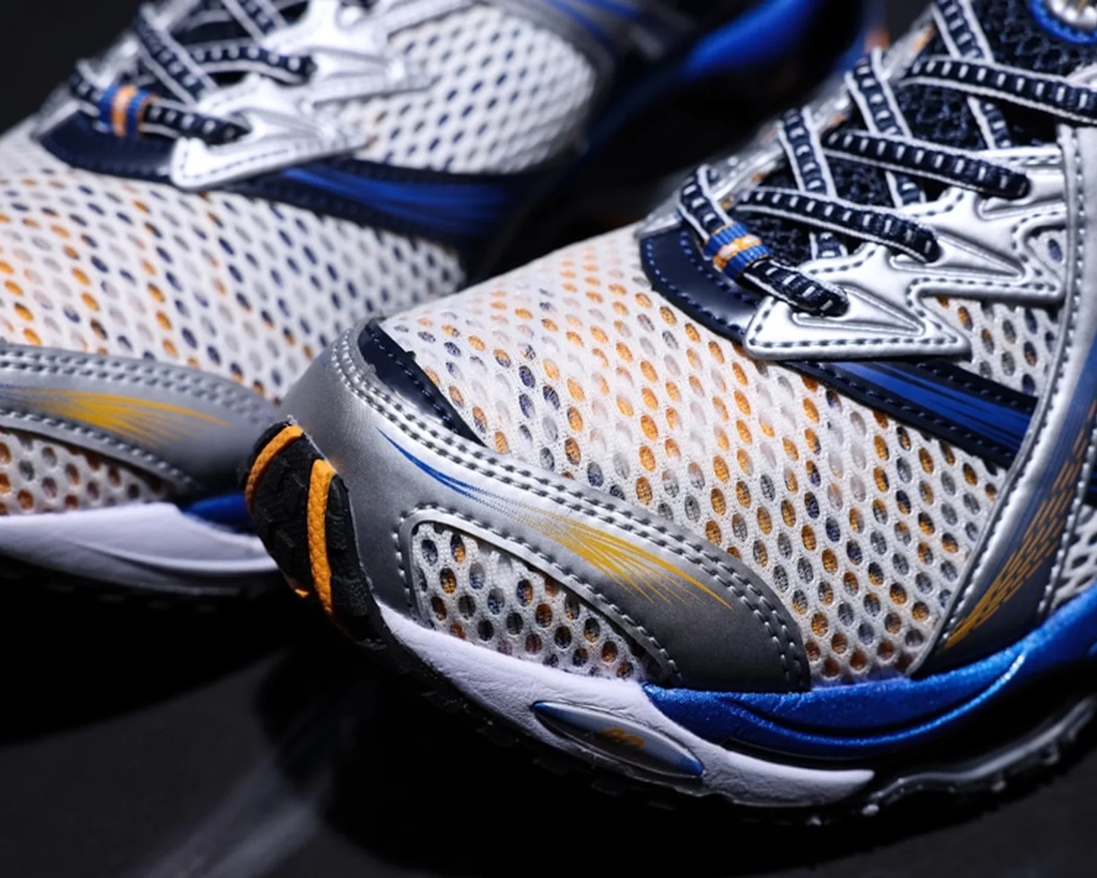 Close-up of white and blue mesh running shoes with silver and orange accents on a black surface.