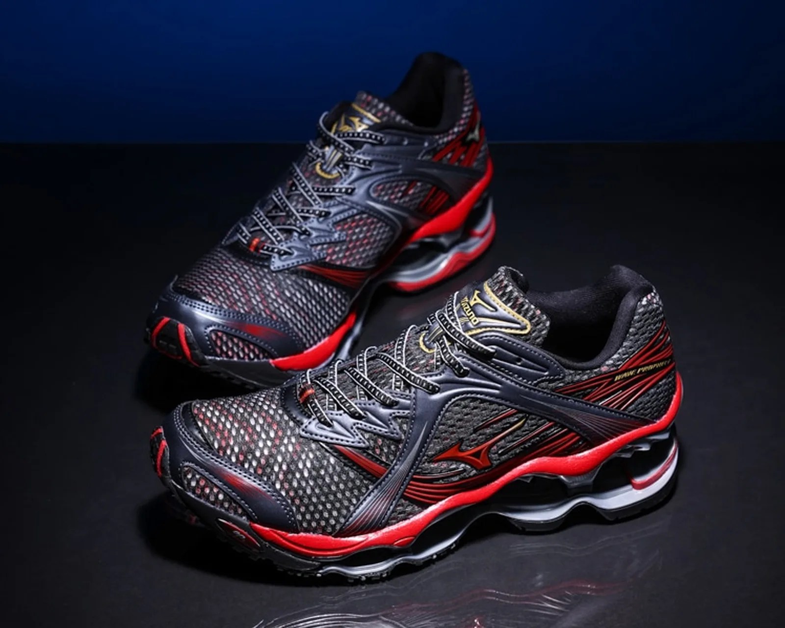 Pair of black and red Mizuno Wave Prophecy running shoes on a dark reflective surface.