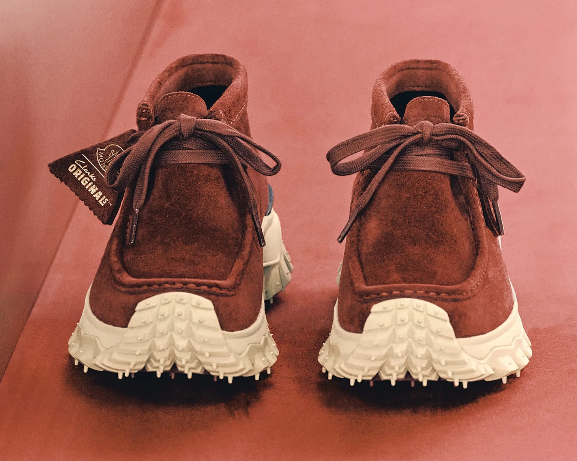 Brown suede Clarks Originals shoes with white textured soles on a reddish surface.