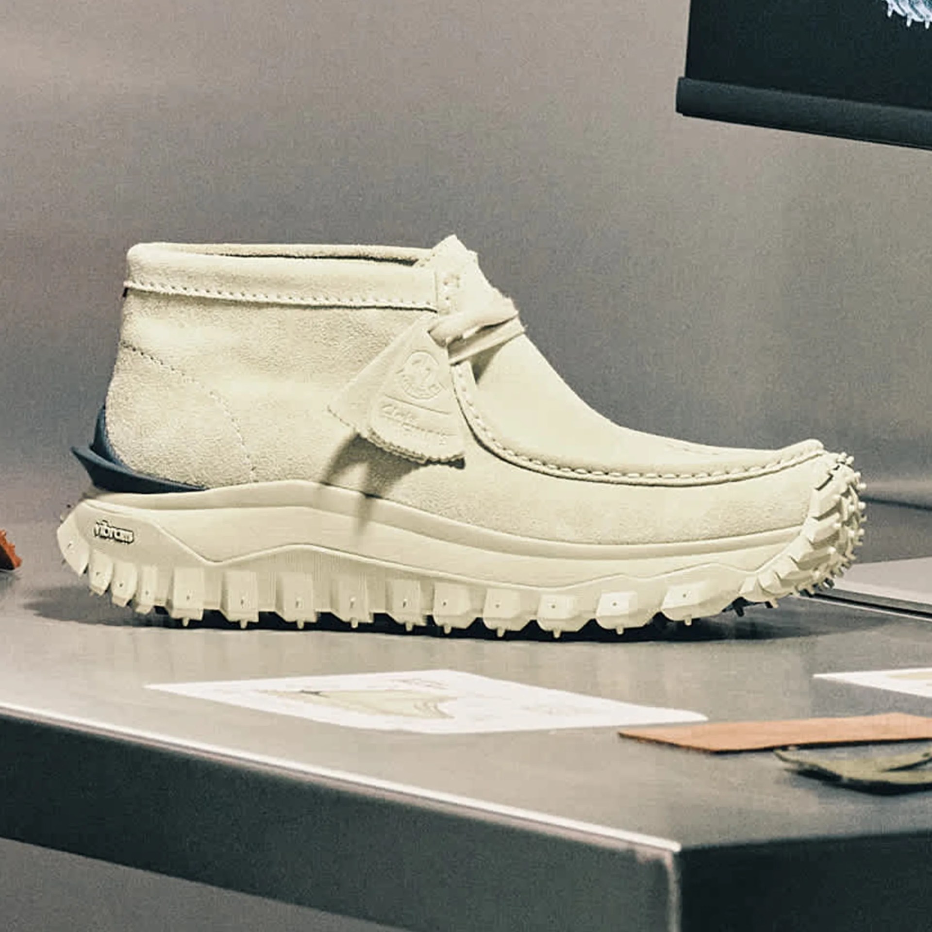 Off-white suede ankle boot with rugged Vibram sole on a gray surface.