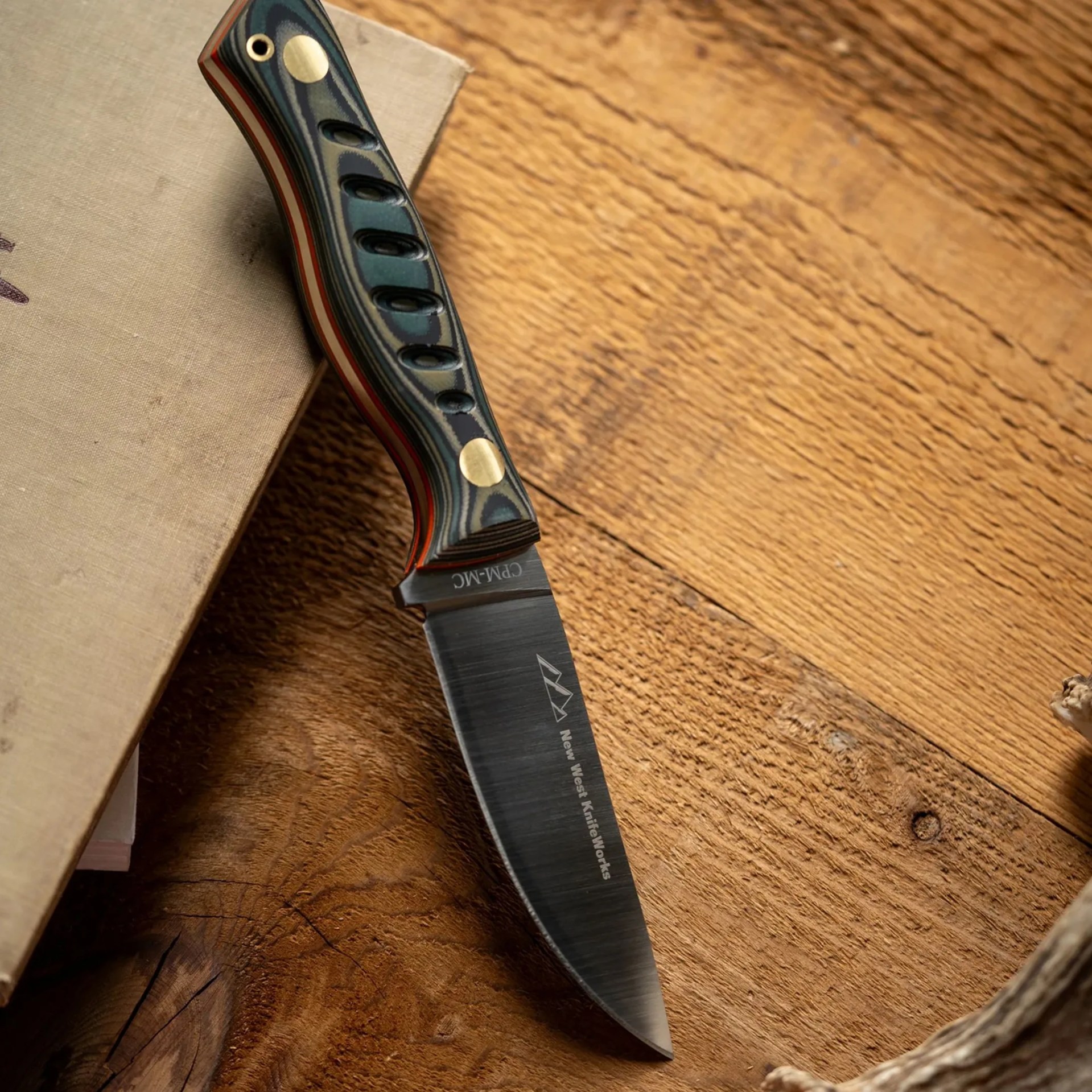 Knife with a black and green textured handle featuring brass rivets, resting on a wooden surface.