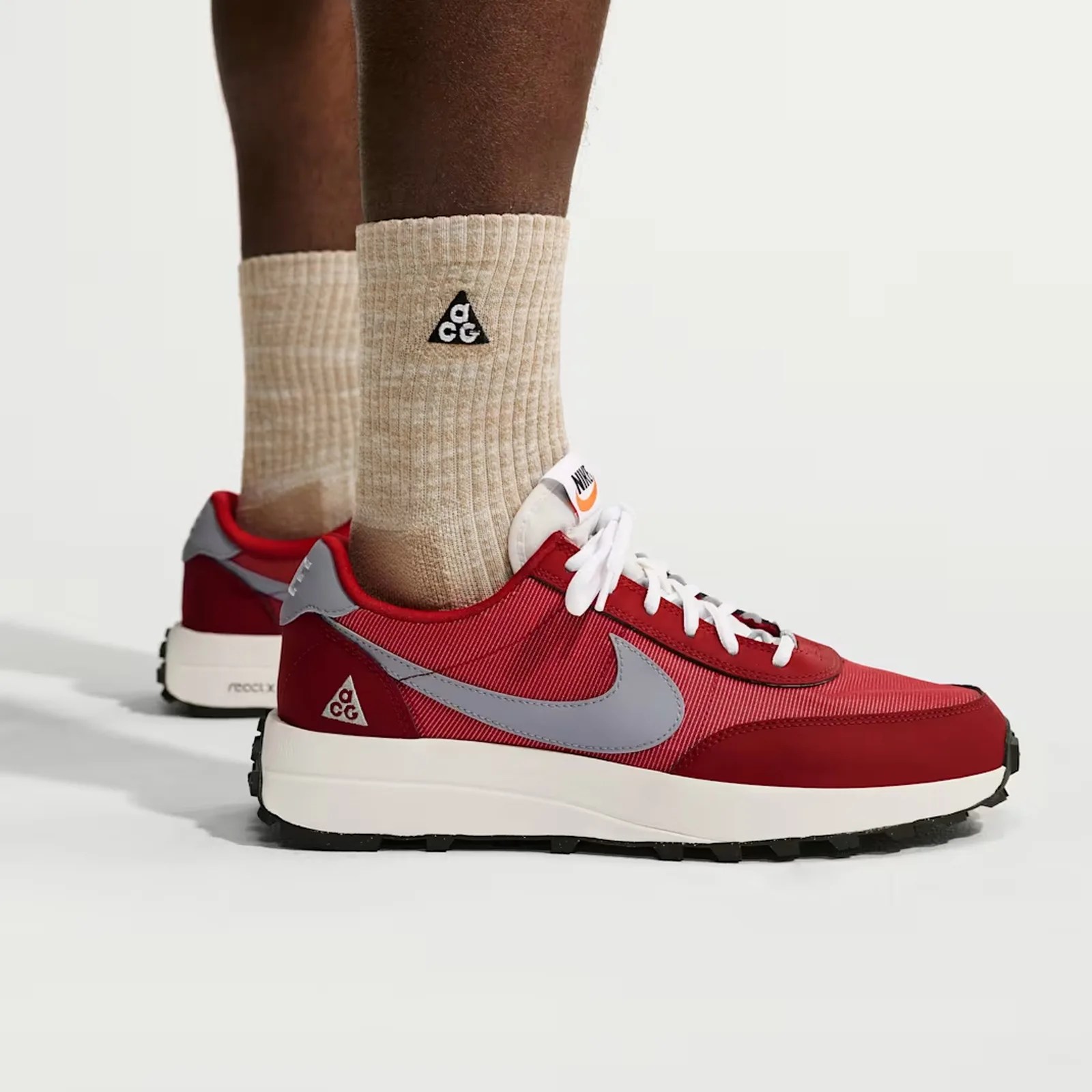Red Nike sneakers with gray swoosh and beige ribbed socks featuring a black triangle ACG logo.