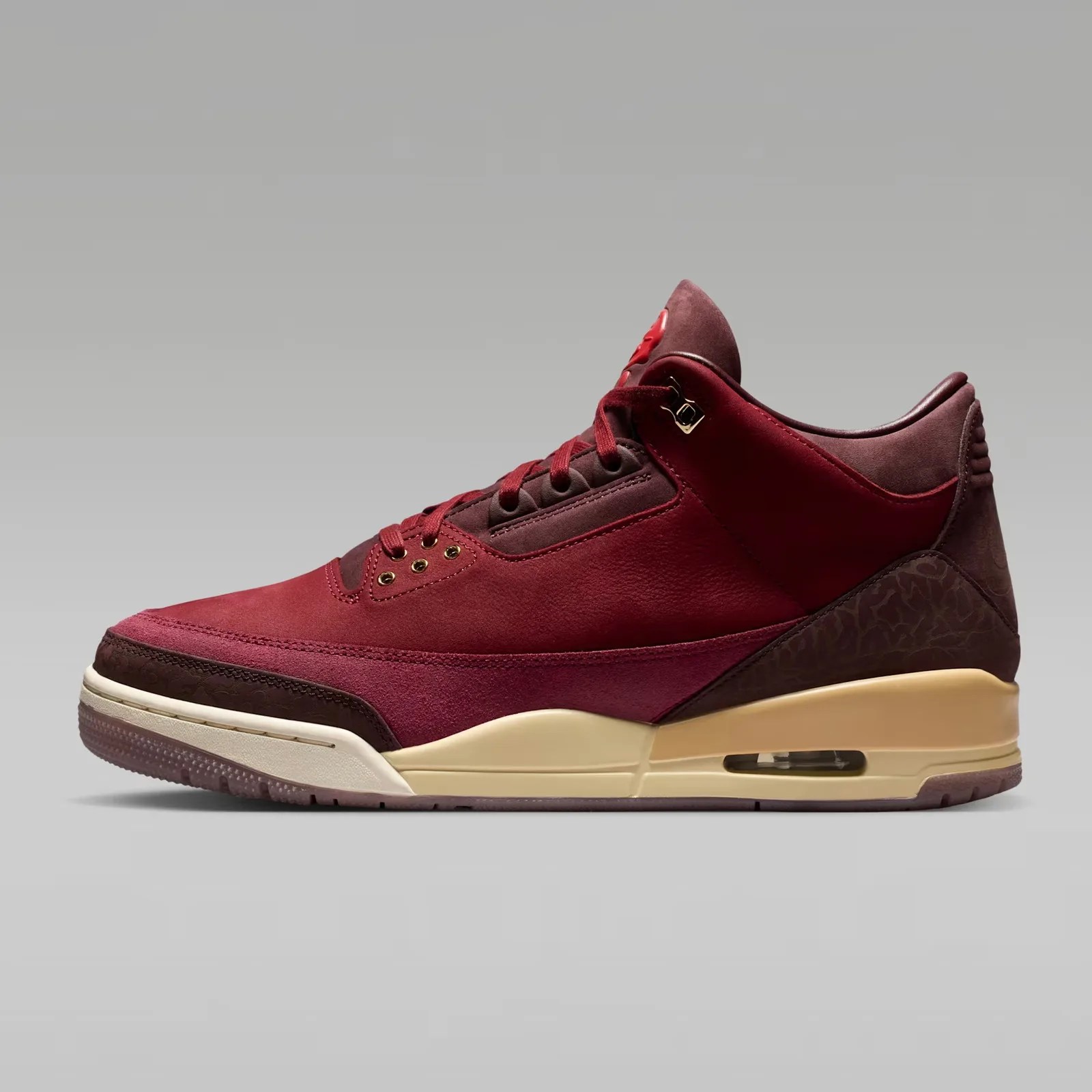 Maroon and burgundy suede sneaker with cream midsole and visible air unit on a gray background.