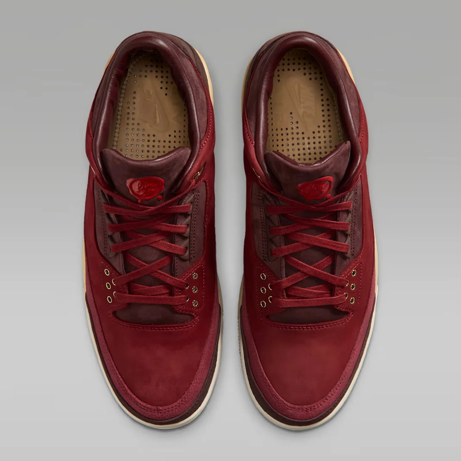 Pair of red leather sneakers with maroon accents and perforated tan insoles on a gray background.