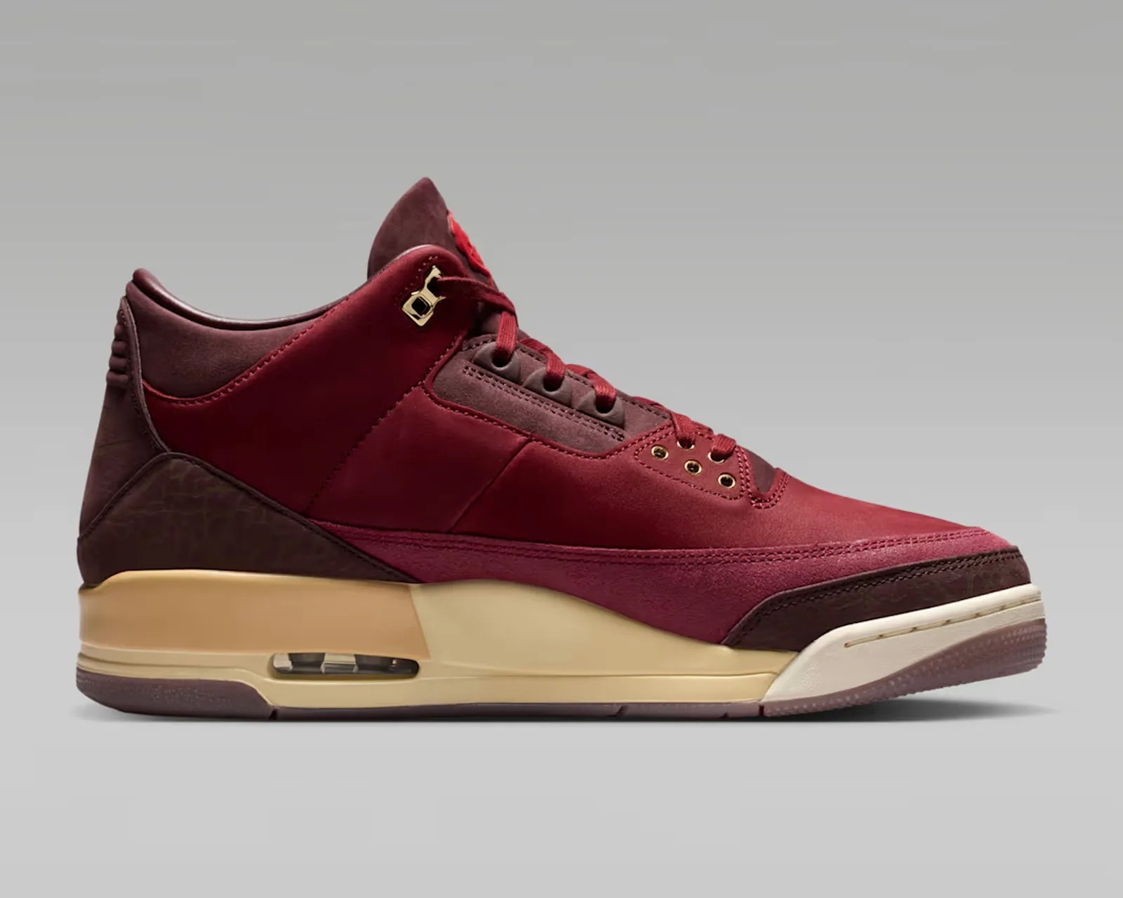 Maroon and burgundy suede sneaker with beige midsole and visible air unit on gray background.