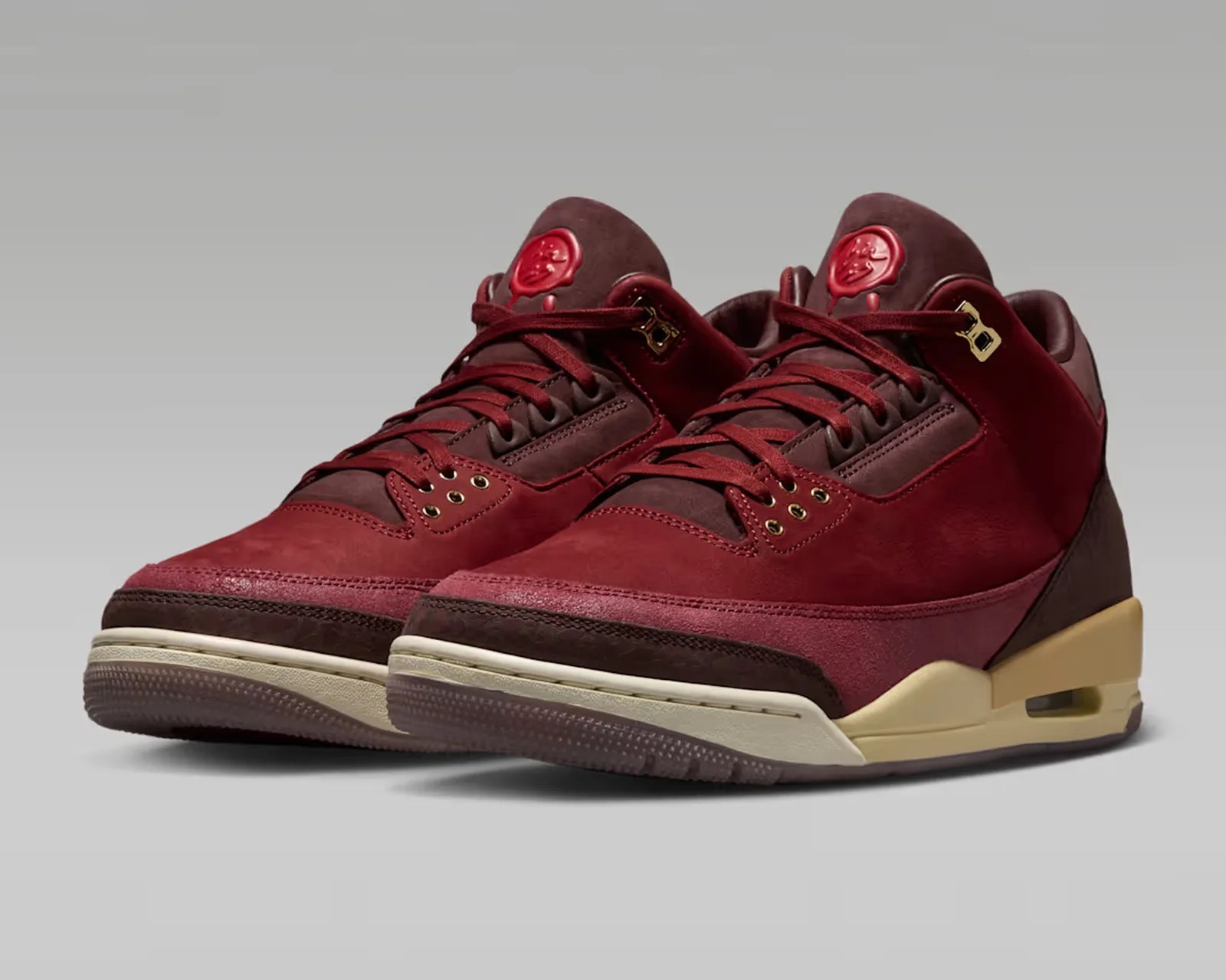 Pair of maroon and burgundy high-top sneakers with gold eyelets and beige midsoles on a gray background.