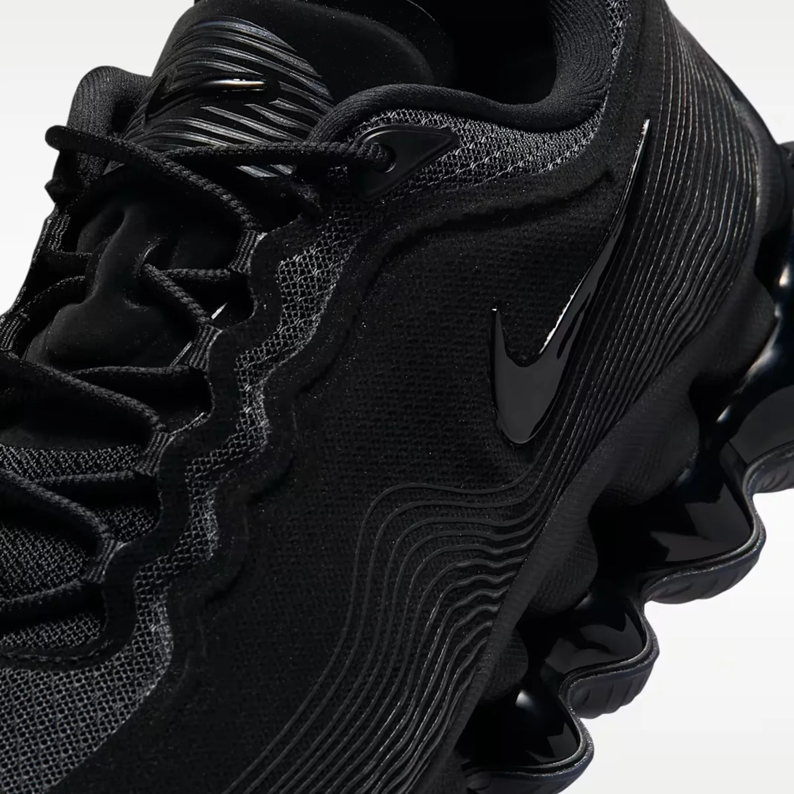 Close-up of a black Nike sneaker with textured mesh upper, glossy black swoosh, and segmented sole.
