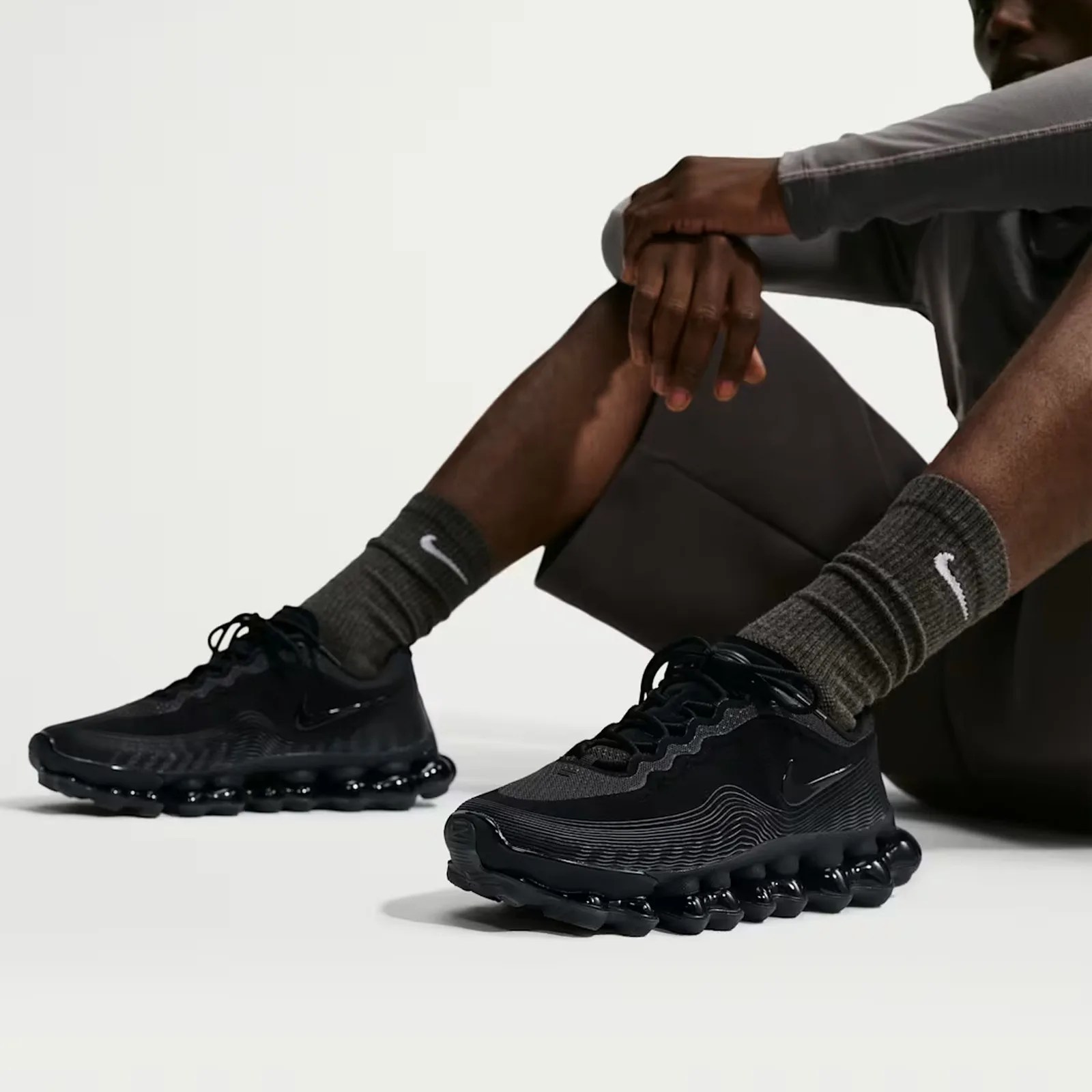Black Nike sneakers with wavy design and bubble sole worn with dark gray Nike socks.