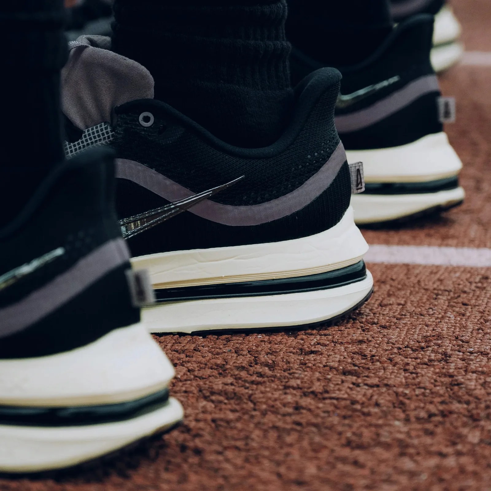Black and gray Nike running shoes with white soles on a textured brown track surface.