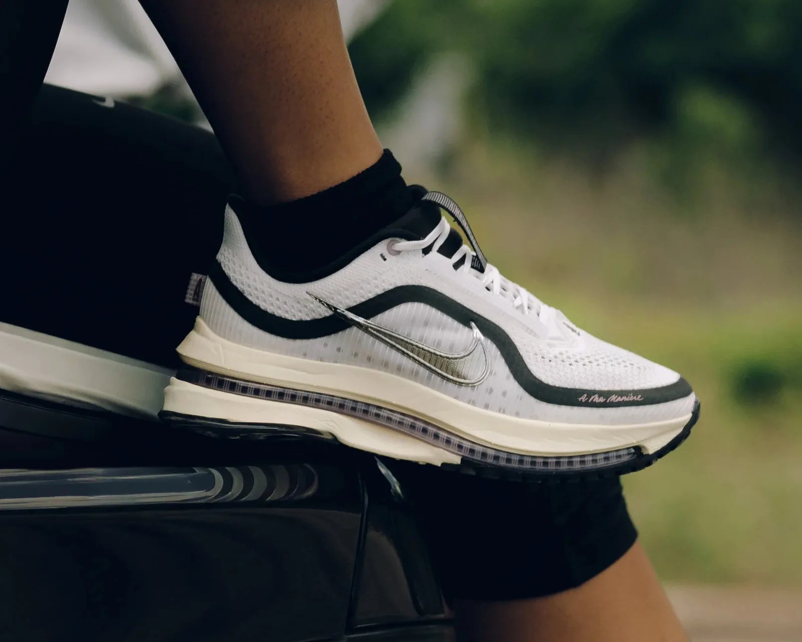White and black Nike running shoe with visible air sole worn by a person sitting outdoors.