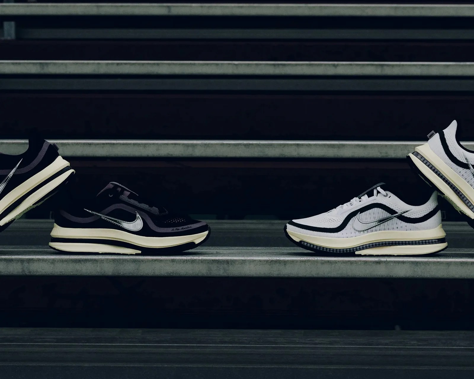 Two pairs of Nike running shoes, one black and one white, displayed on concrete steps.