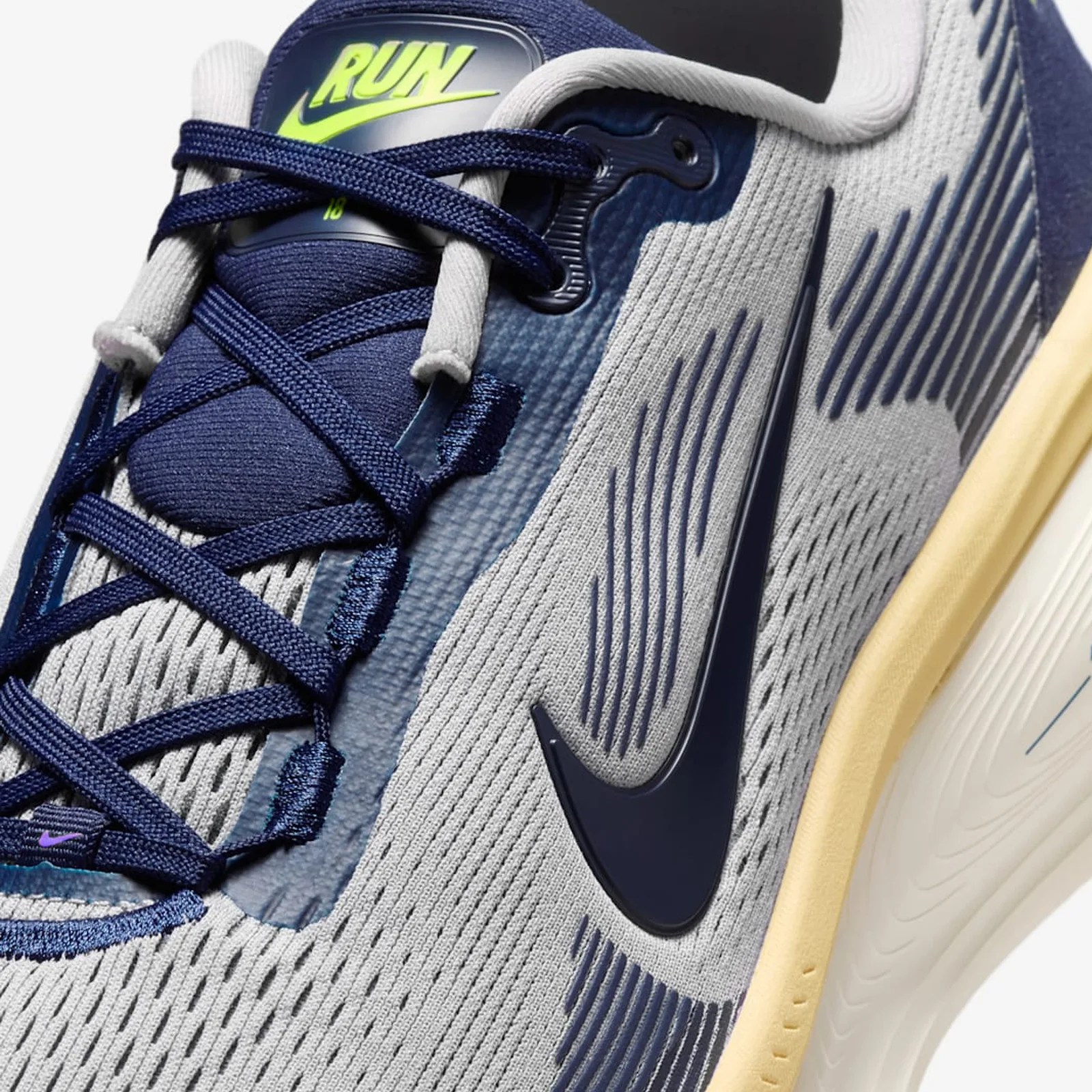 Close-up of a gray and navy Nike running shoe with navy laces, a yellow sole, and a "RUN" label on the tongue.