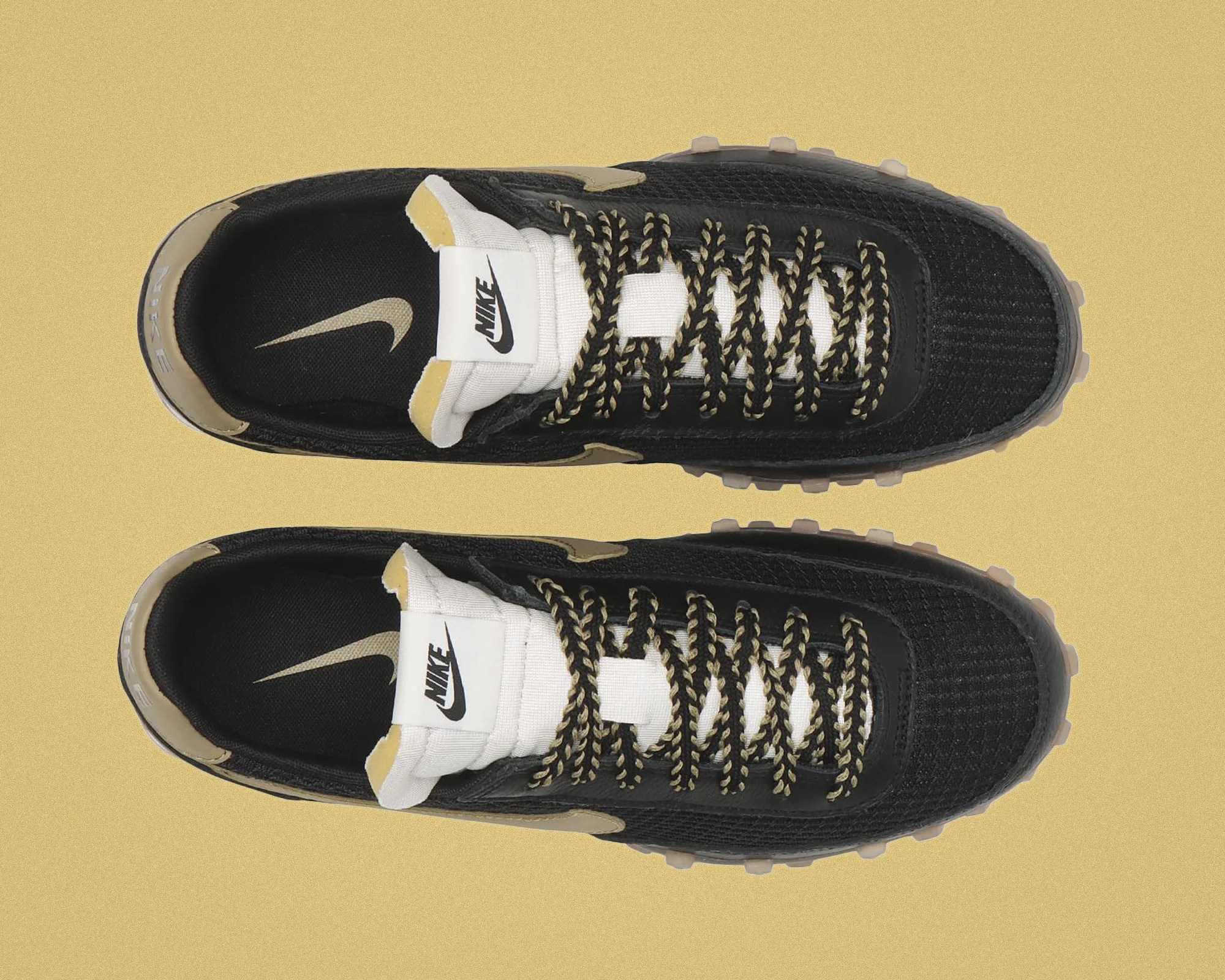 Top view of black and beige Nike sneakers with white tongue and black-and-beige braided laces on a beige background.