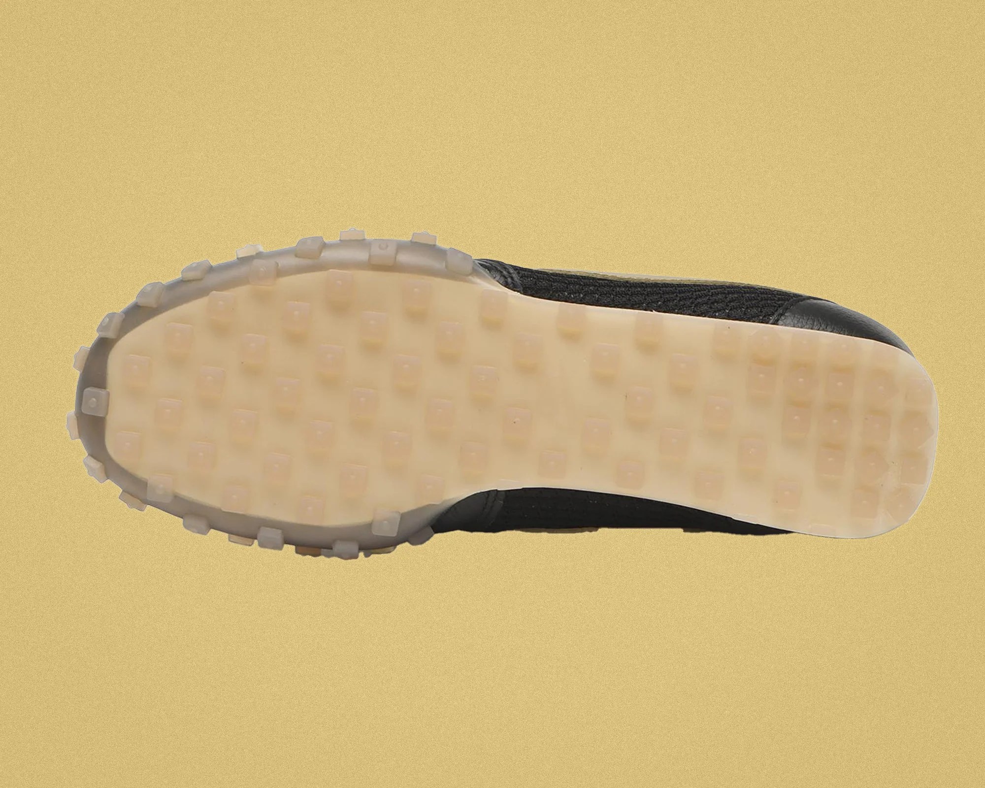 Shoe sole with translucent rubber studs and black upper edge on a beige background.