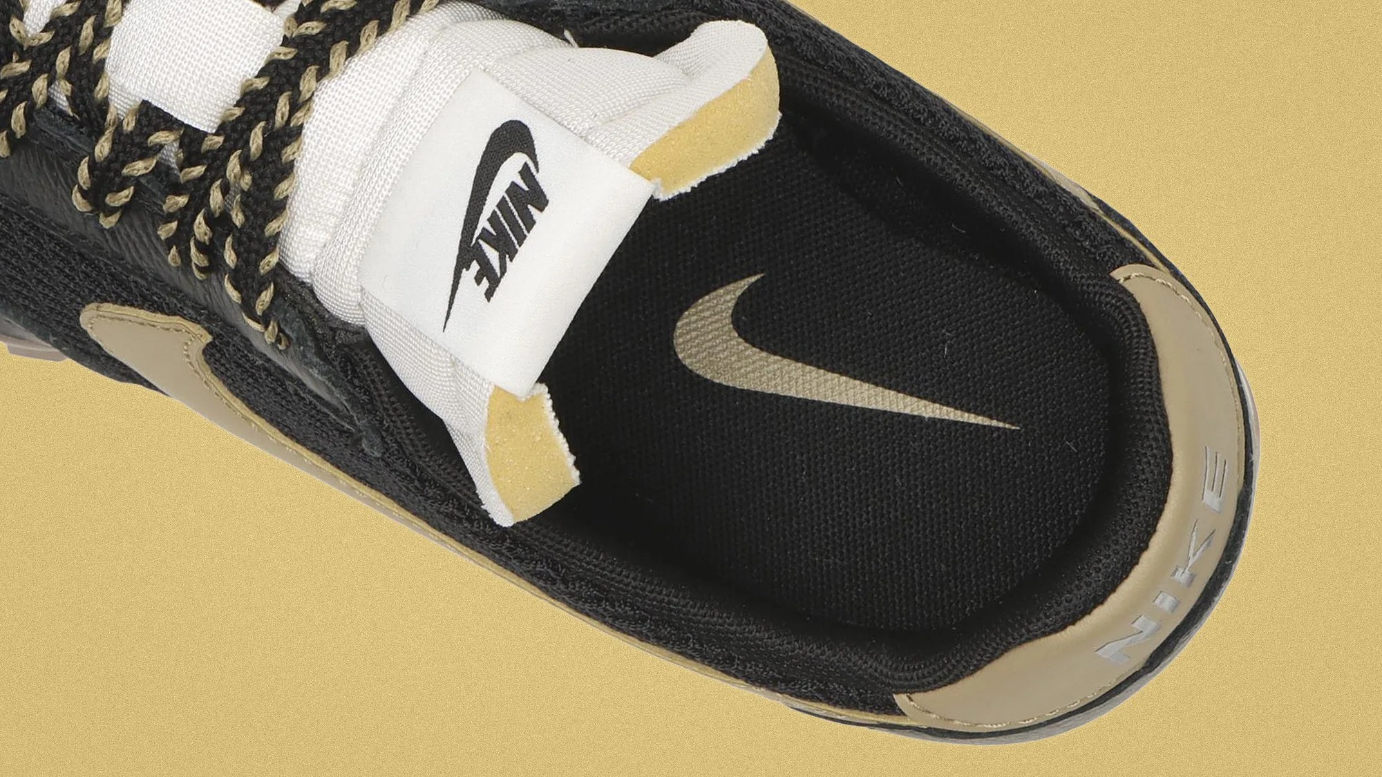 Top view of a black and beige Nike sneaker with black and beige braided laces and a white tongue label featuring the Nike logo.