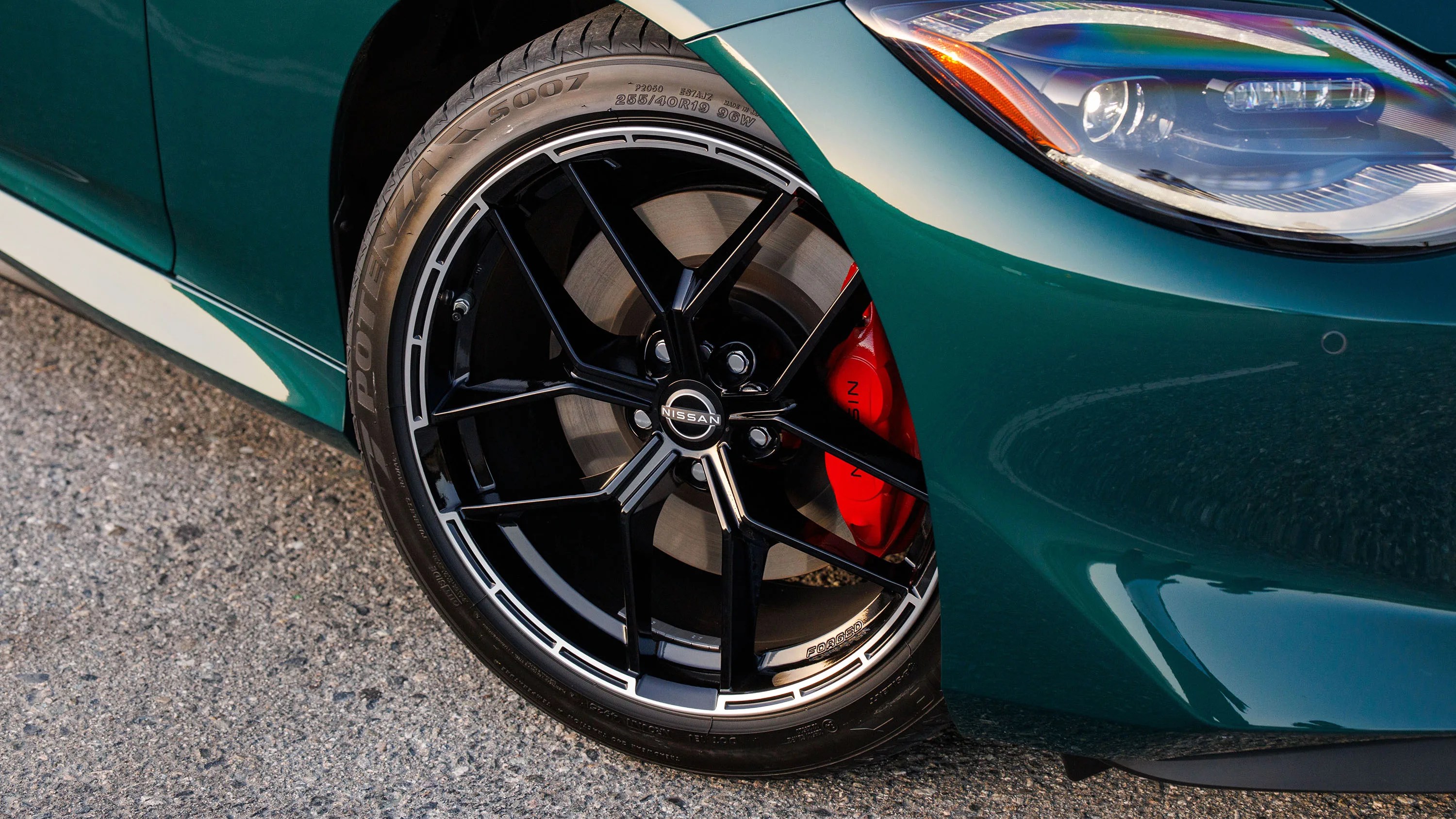 Close-up of a black Nissan alloy wheel with red brake caliper on a green car.