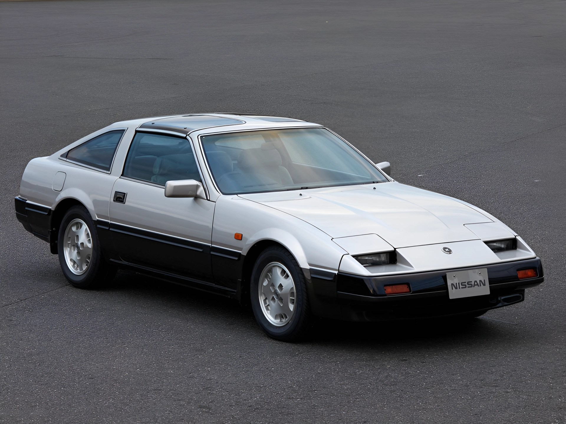 Two-tone white and black Nissan sports car with pop-up headlights parked on asphalt.