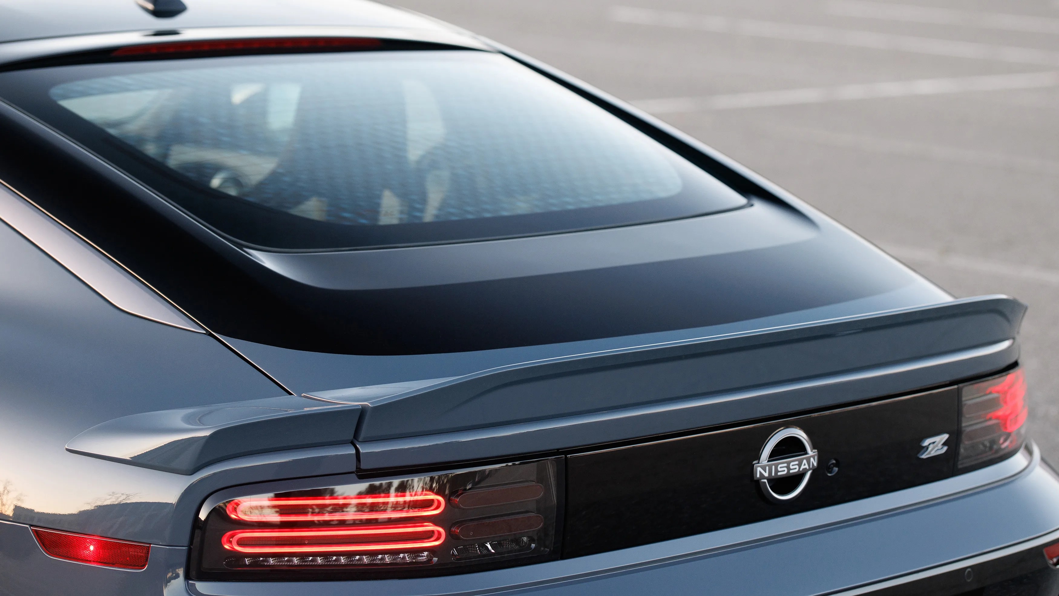 Rear view of a dark gray Nissan Z sports car showing the rear window, spoiler, and illuminated taillights.