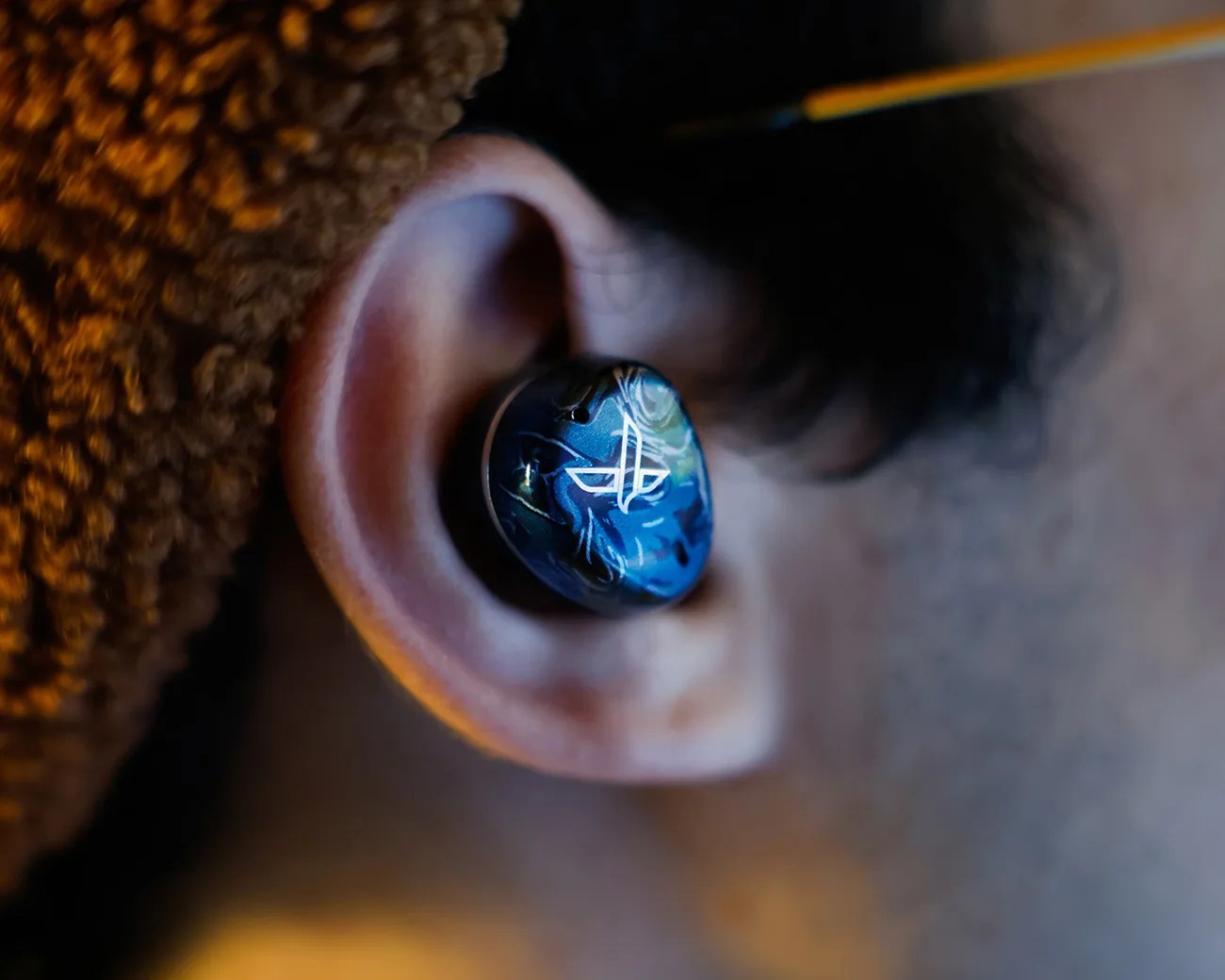 Blue wireless earbud with a white PlayStation logo worn in an ear.