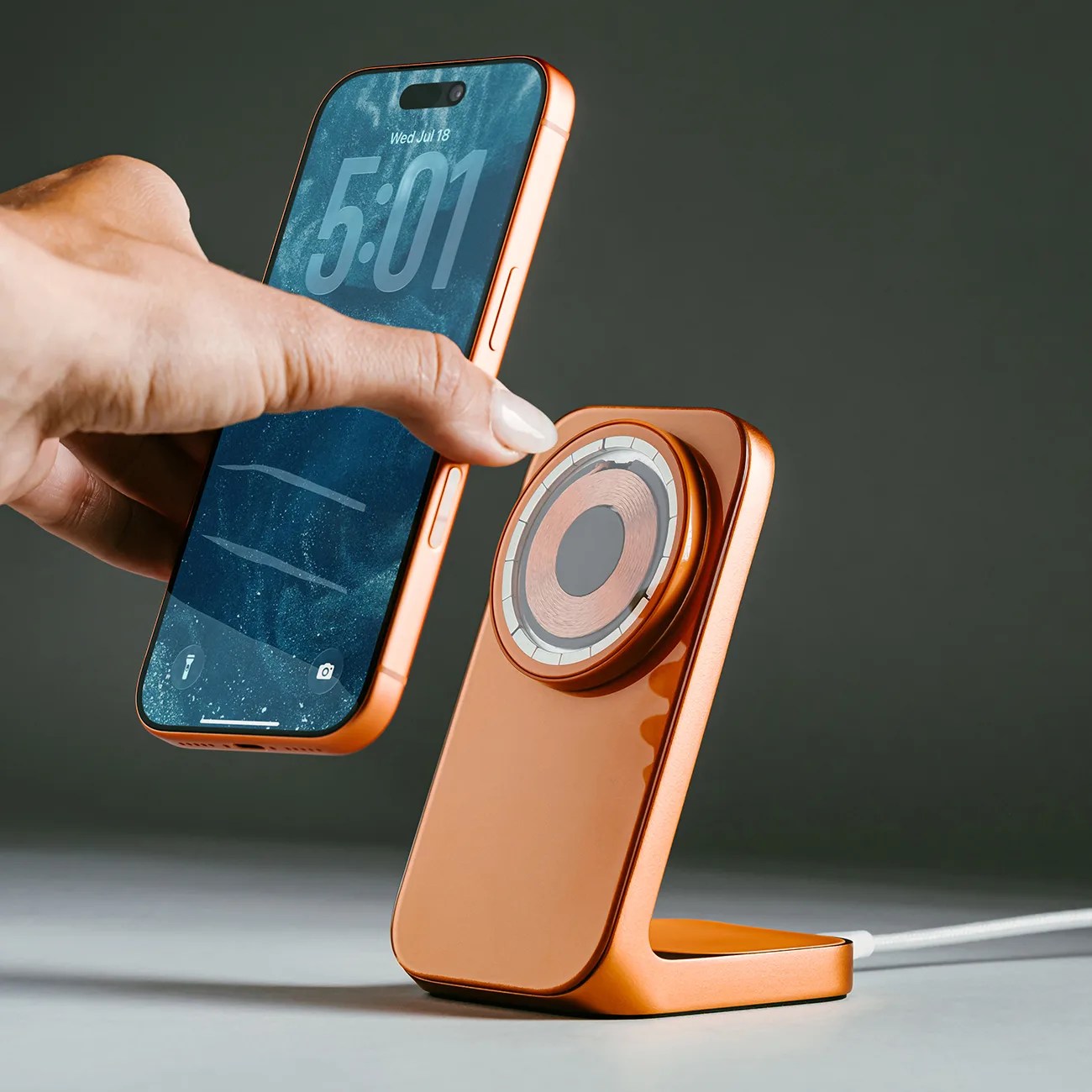 Copper-colored wireless charging stand with a matching smartphone being placed on it by a hand.