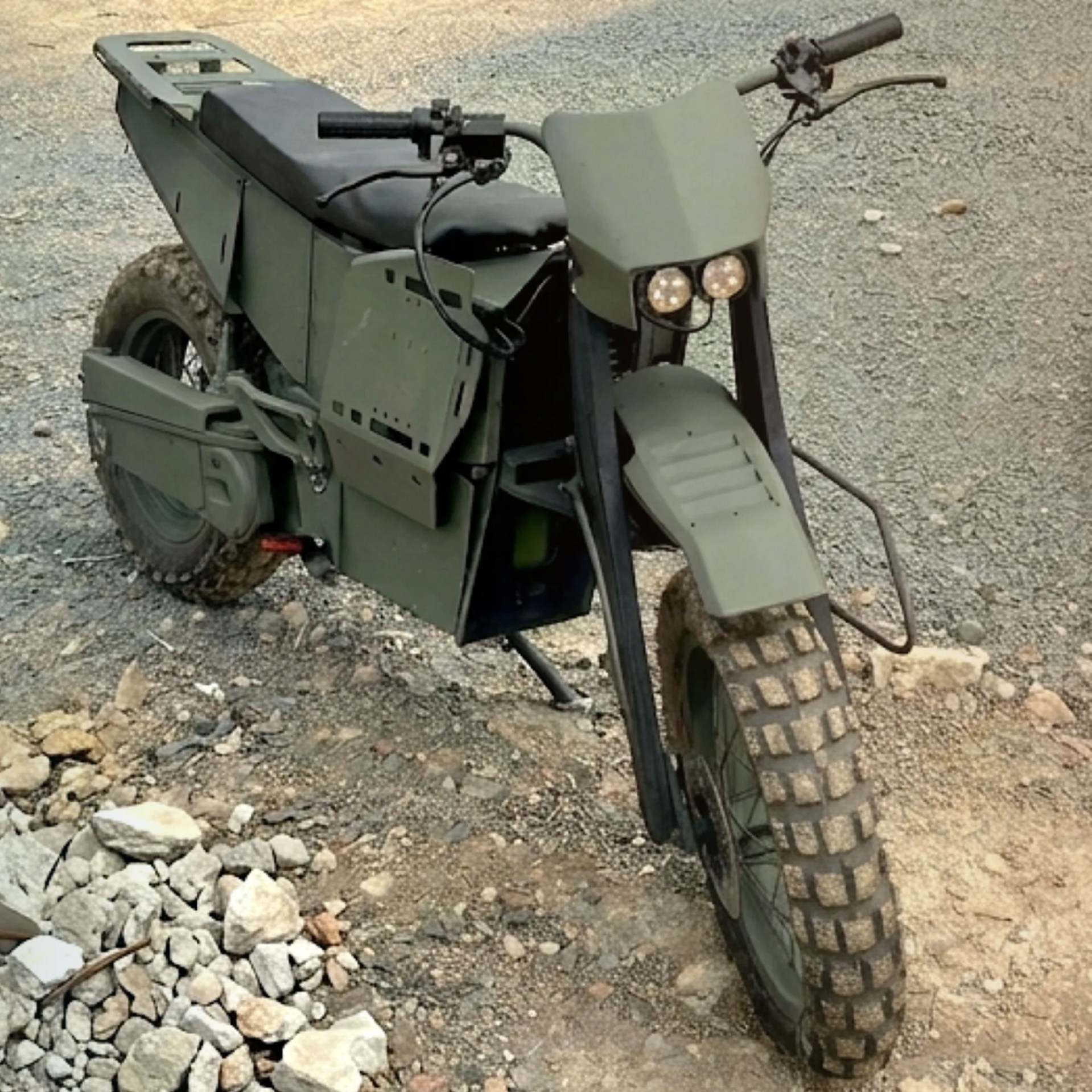 Military-style green off-road motorcycle with knobby tires on rocky terrain.