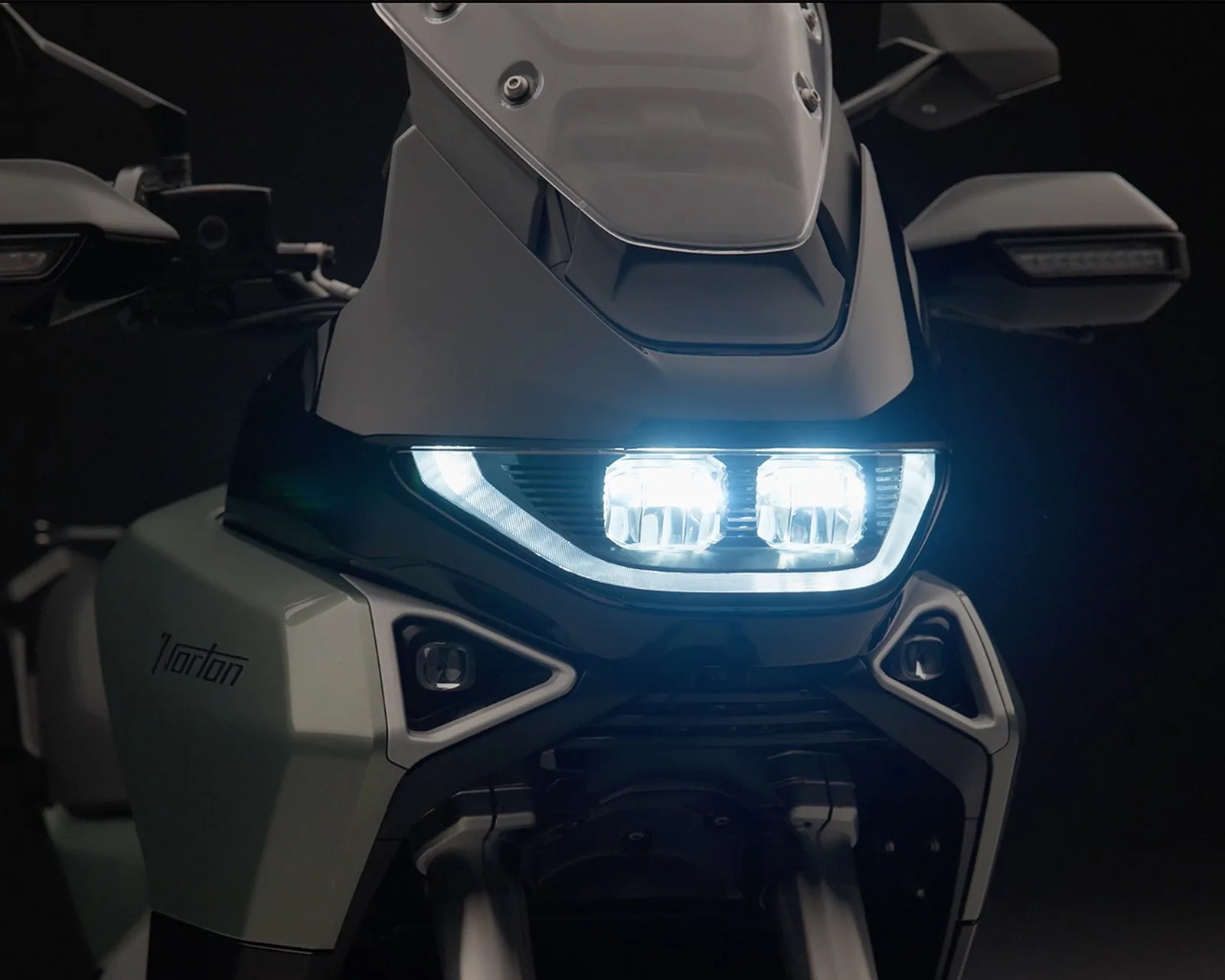 Close-up of a motorcycle front with dual LED headlights and a windshield, showing the "Norton" logo on the side panel.