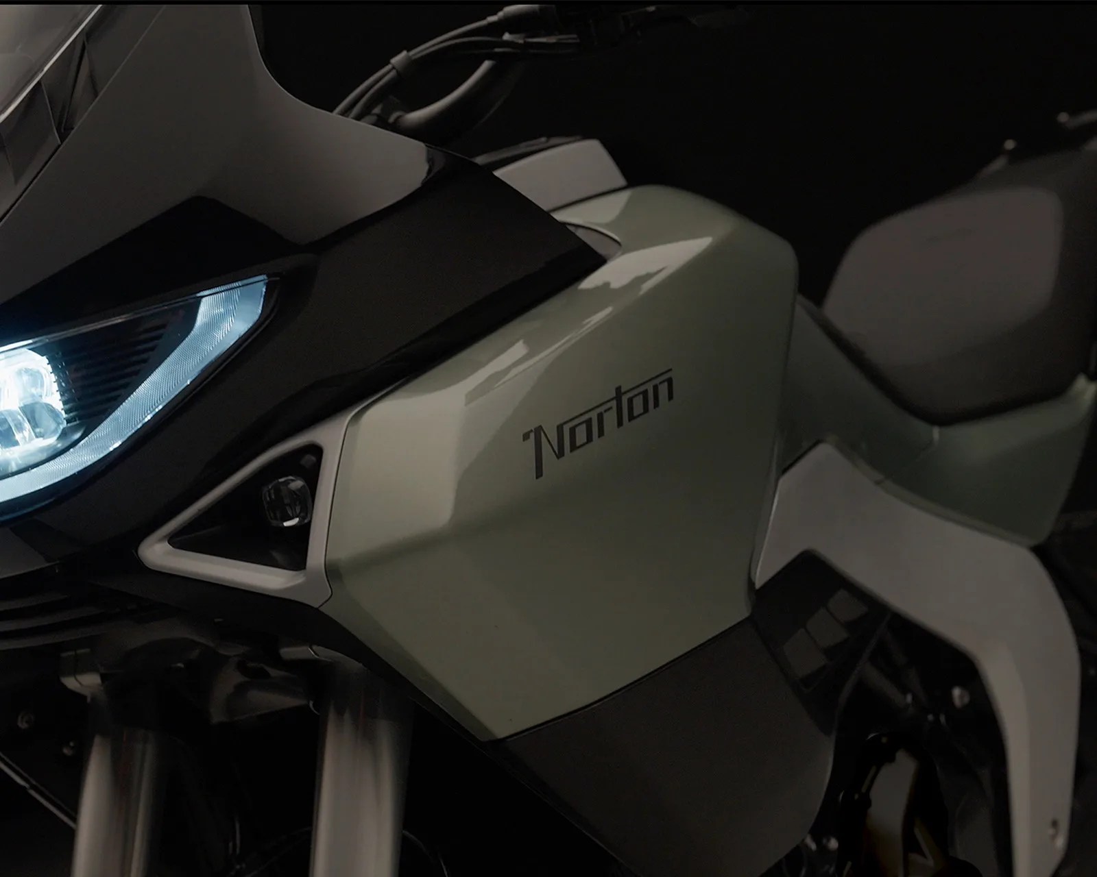 Close-up of a Norton motorcycle's front side panel and headlight with a matte green and black finish.