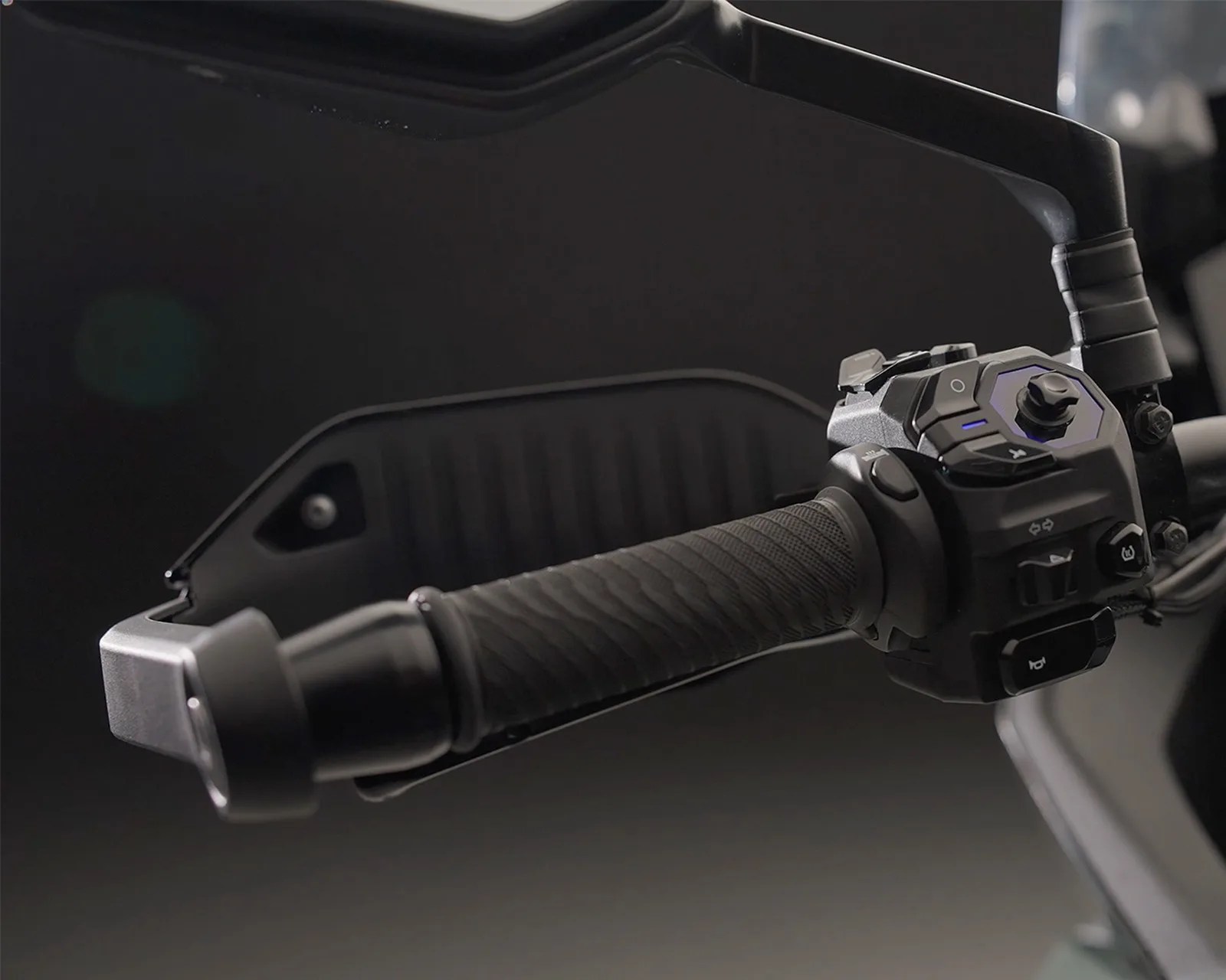 Close-up of a black motorcycle handlebar grip with control switches and a handguard.