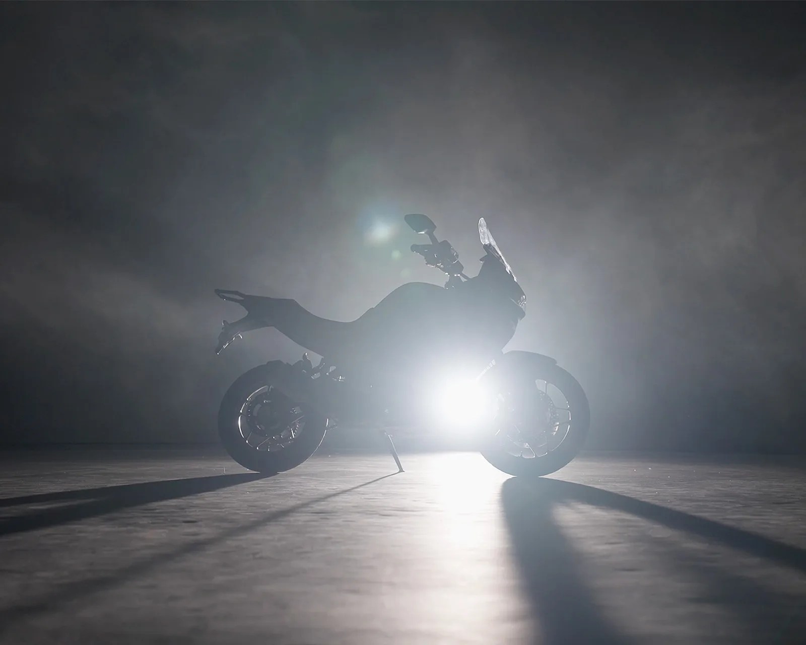 Silhouette of a motorcycle with a bright light behind it casting long shadows on the ground.