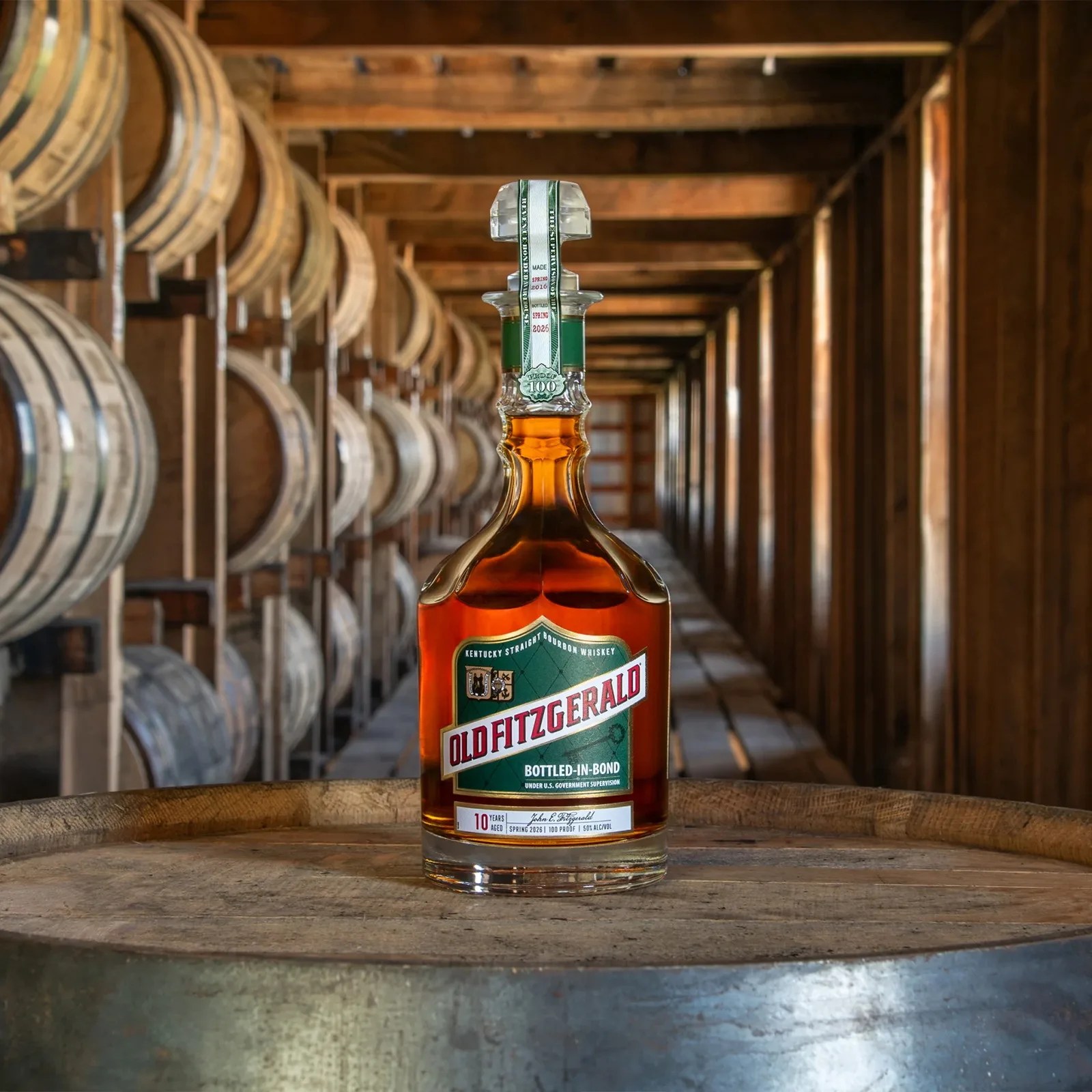Bottle of Old Fitzgerald bourbon whiskey on a wooden barrel with rows of aging barrels in the background.