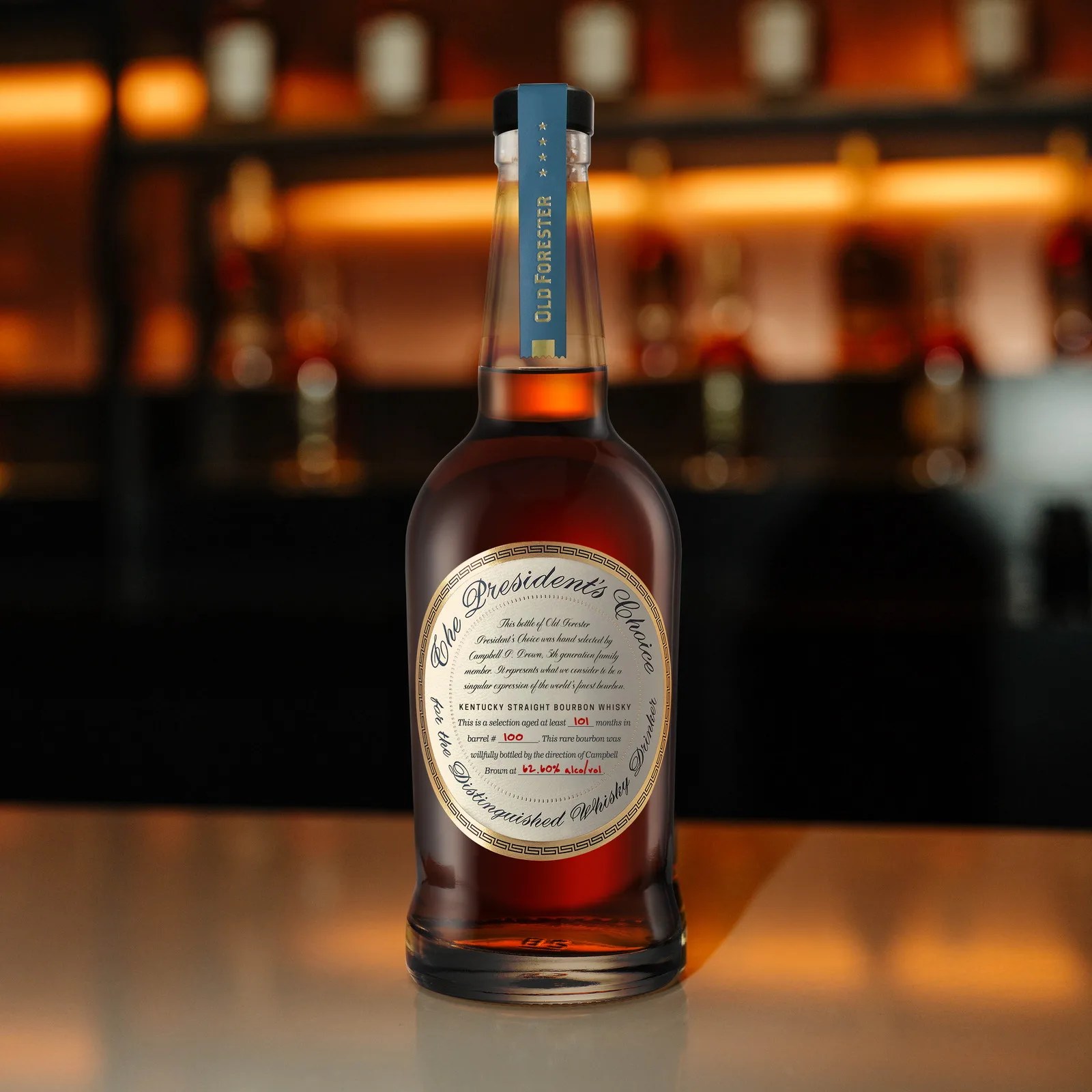 Bottle of Old Forester President's Choice Kentucky Straight Bourbon Whisky on a reflective surface with blurred bar background.