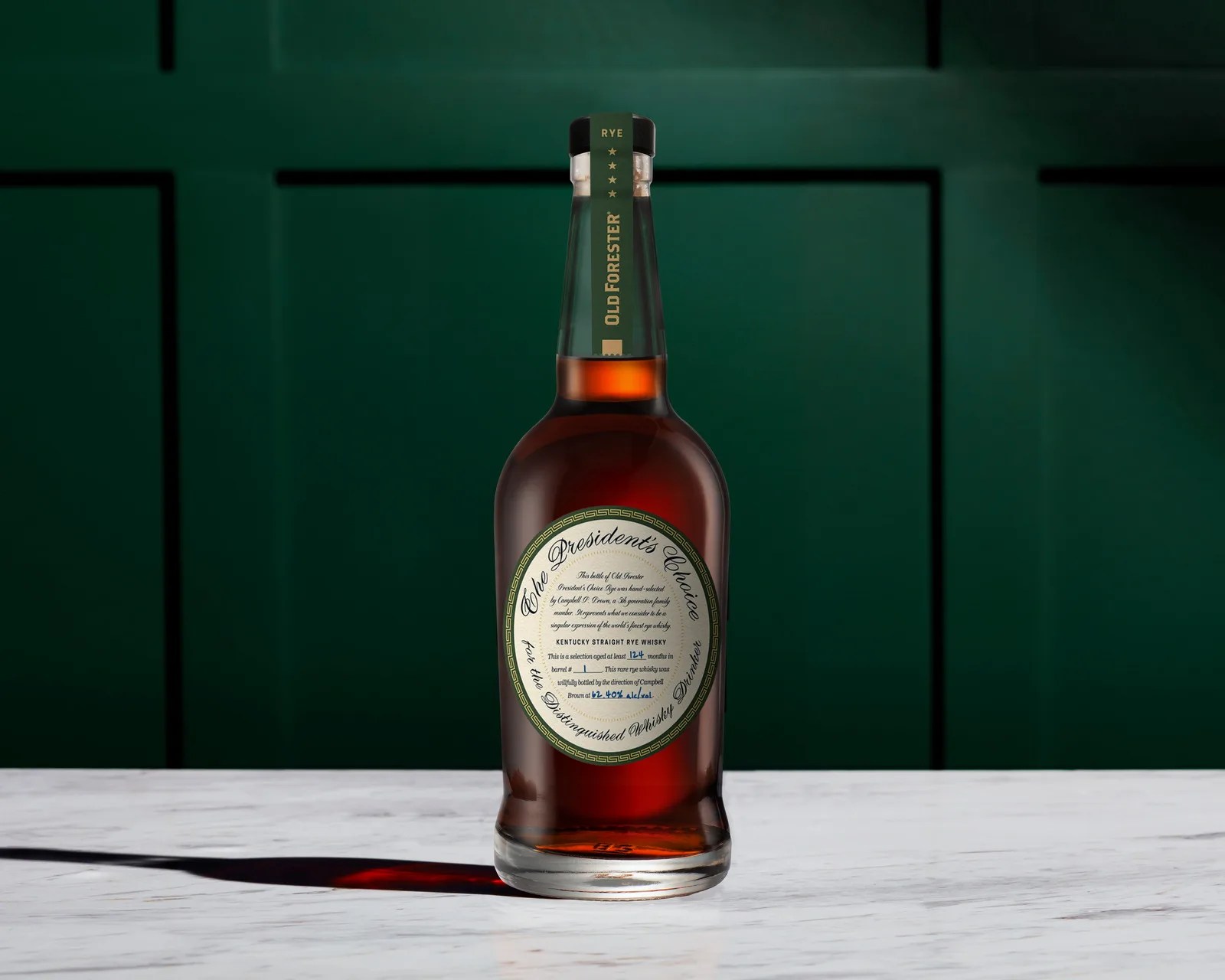 Bottle of Old Forester President's Choice Kentucky Straight Rye Whisky on a white marble surface with a dark green paneled background.