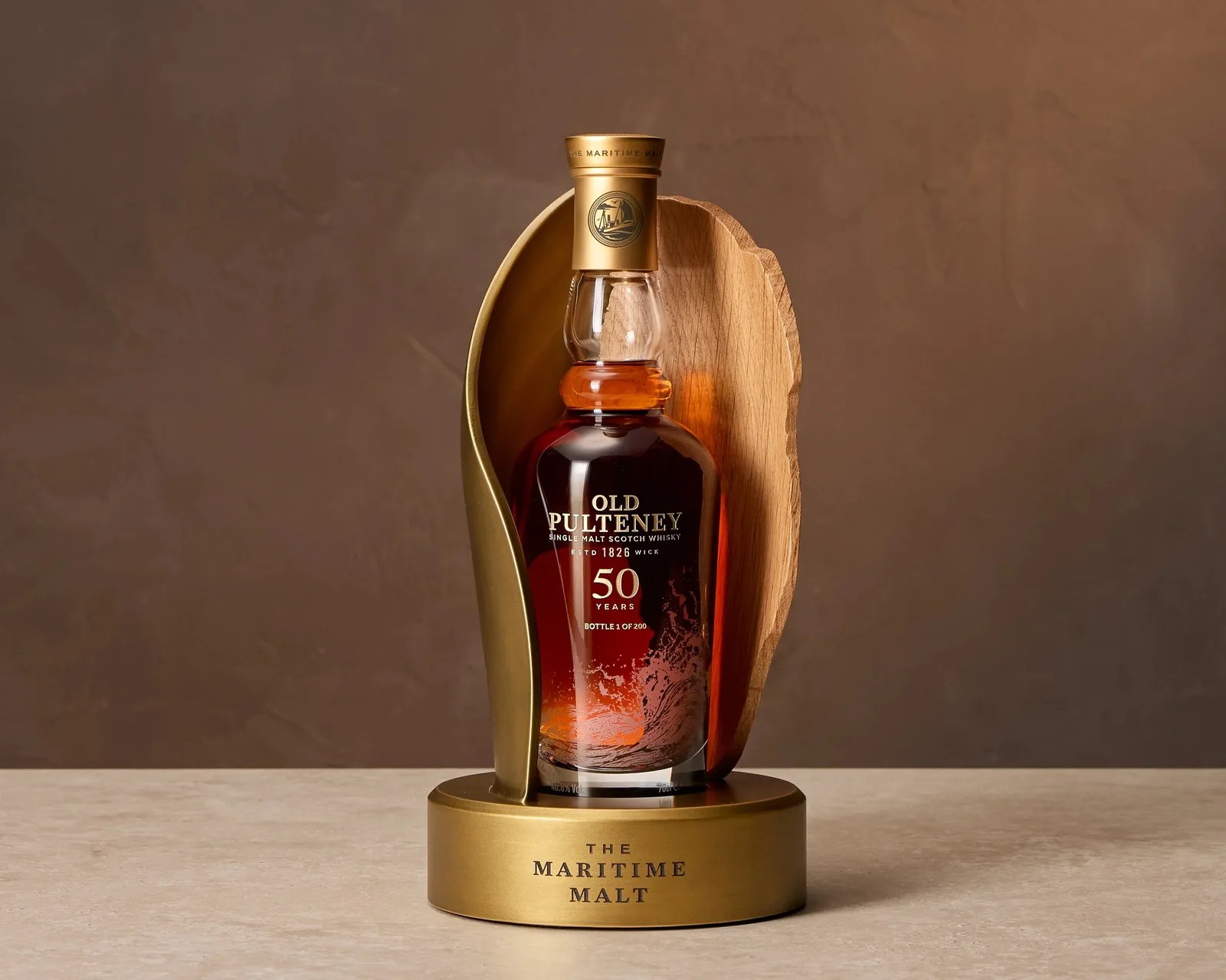 Bottle of Old Pulteney 50 Years single malt Scotch whisky in a gold and wood display stand on a beige surface.