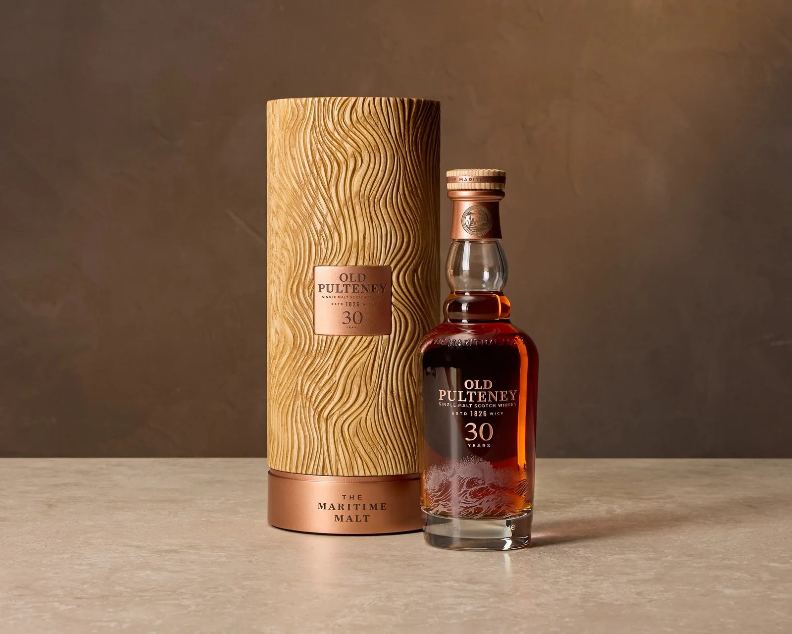 Bottle of Old Pulteney 30-year single malt Scotch whisky with textured cylindrical wooden box on a beige surface.