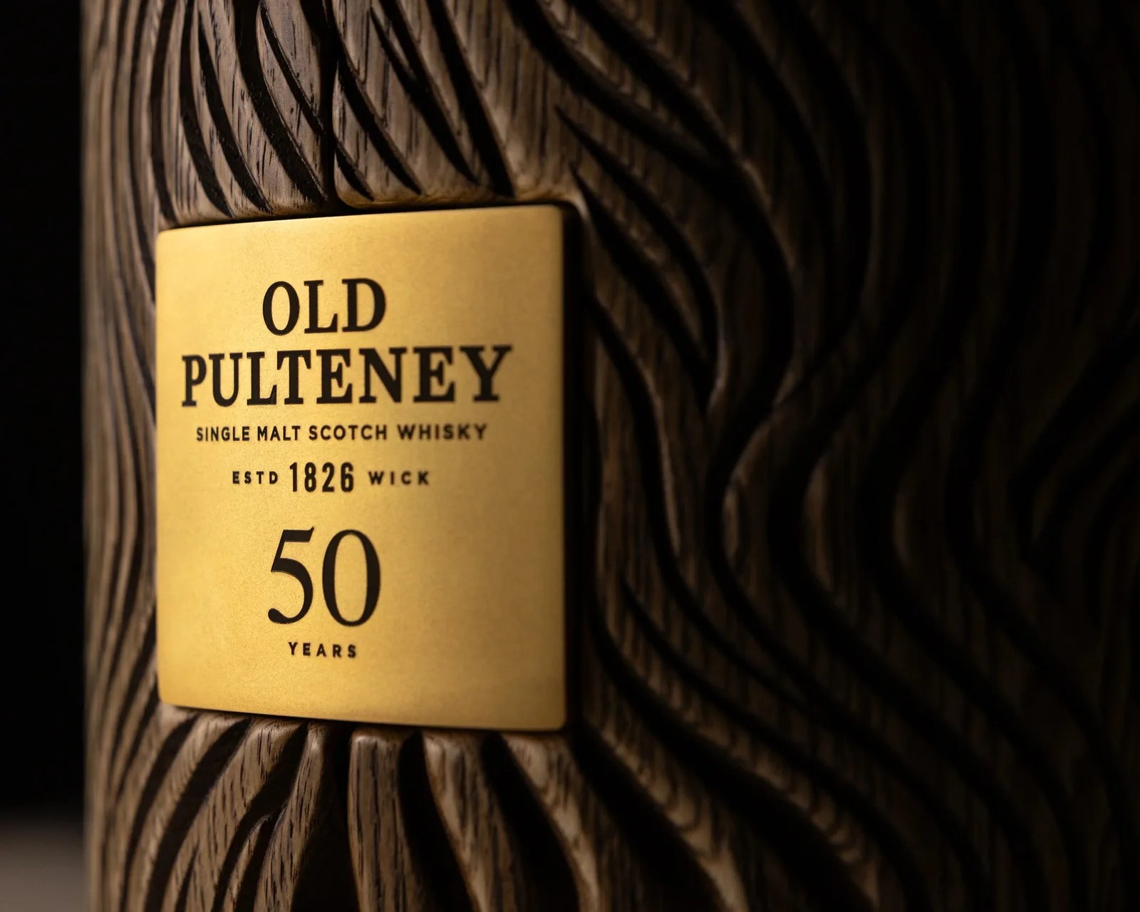 Close-up of a textured wooden container with a gold label reading "Old Pulteney Single Malt Scotch Whisky 50 Years.