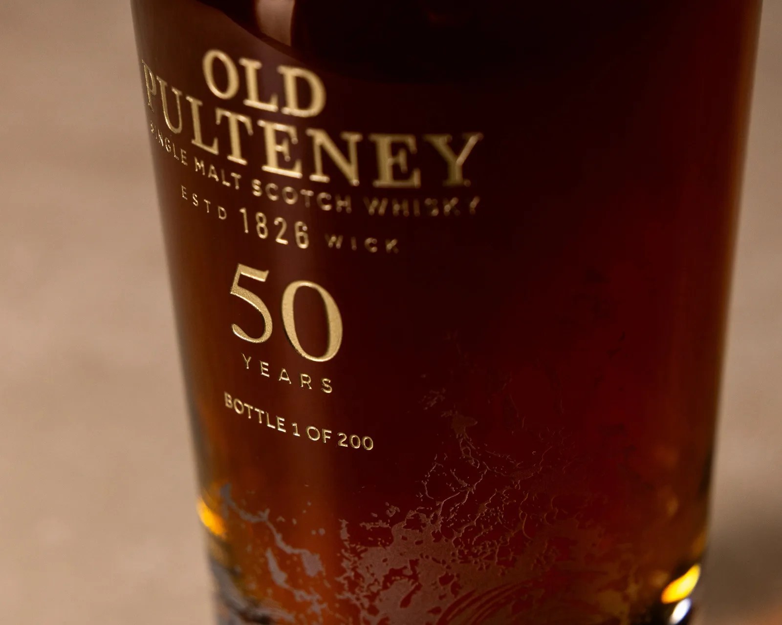 Close-up of a dark amber Old Pulteney 50 years single malt Scotch whisky bottle with gold lettering.
