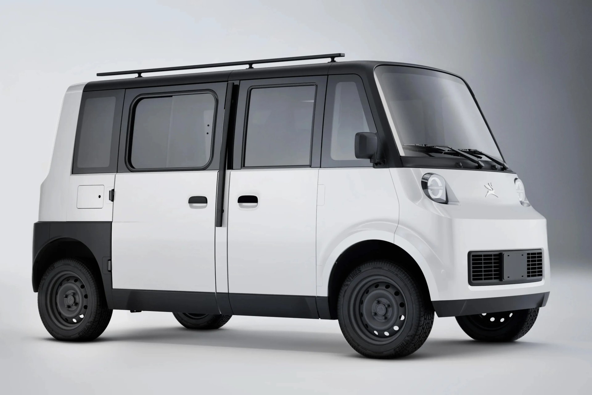 White and black compact electric van with boxy design and roof rails on a gray background.