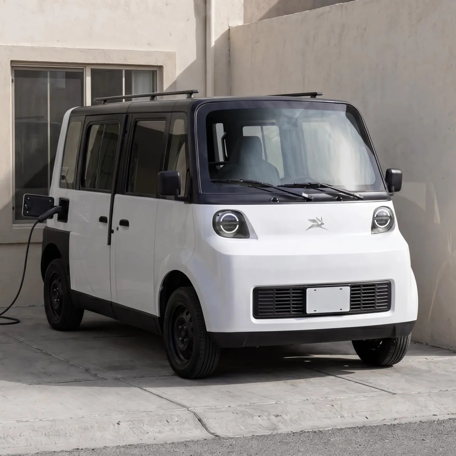 White compact electric car with black roof and round headlights charging near a beige building.