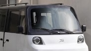 Front view of a white compact electric van with circular LED headlights and black roof rails.