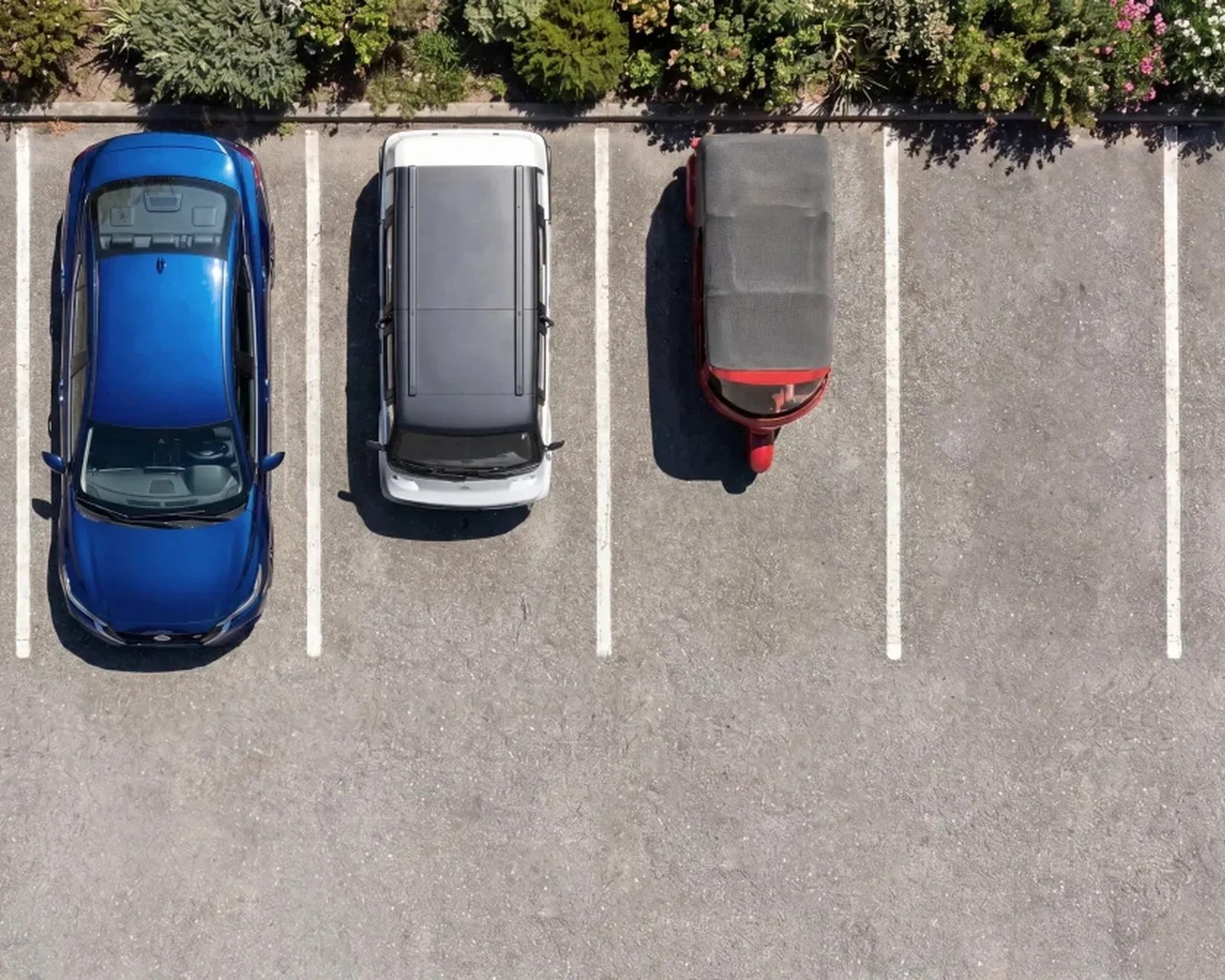 Aerial view of a blue car, a white SUV, and a red three-wheeled vehicle parked in adjacent spaces in a parking lot.