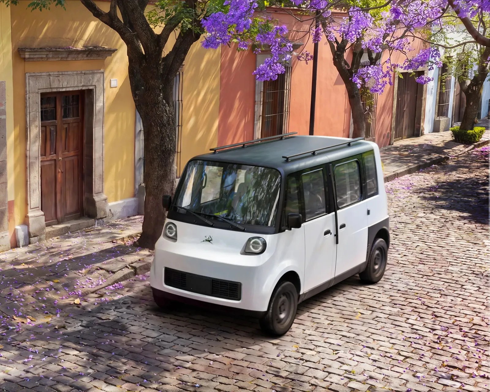 Compact white electric car with black roof and roof rails parked on a cobblestone street under purple flowering trees.