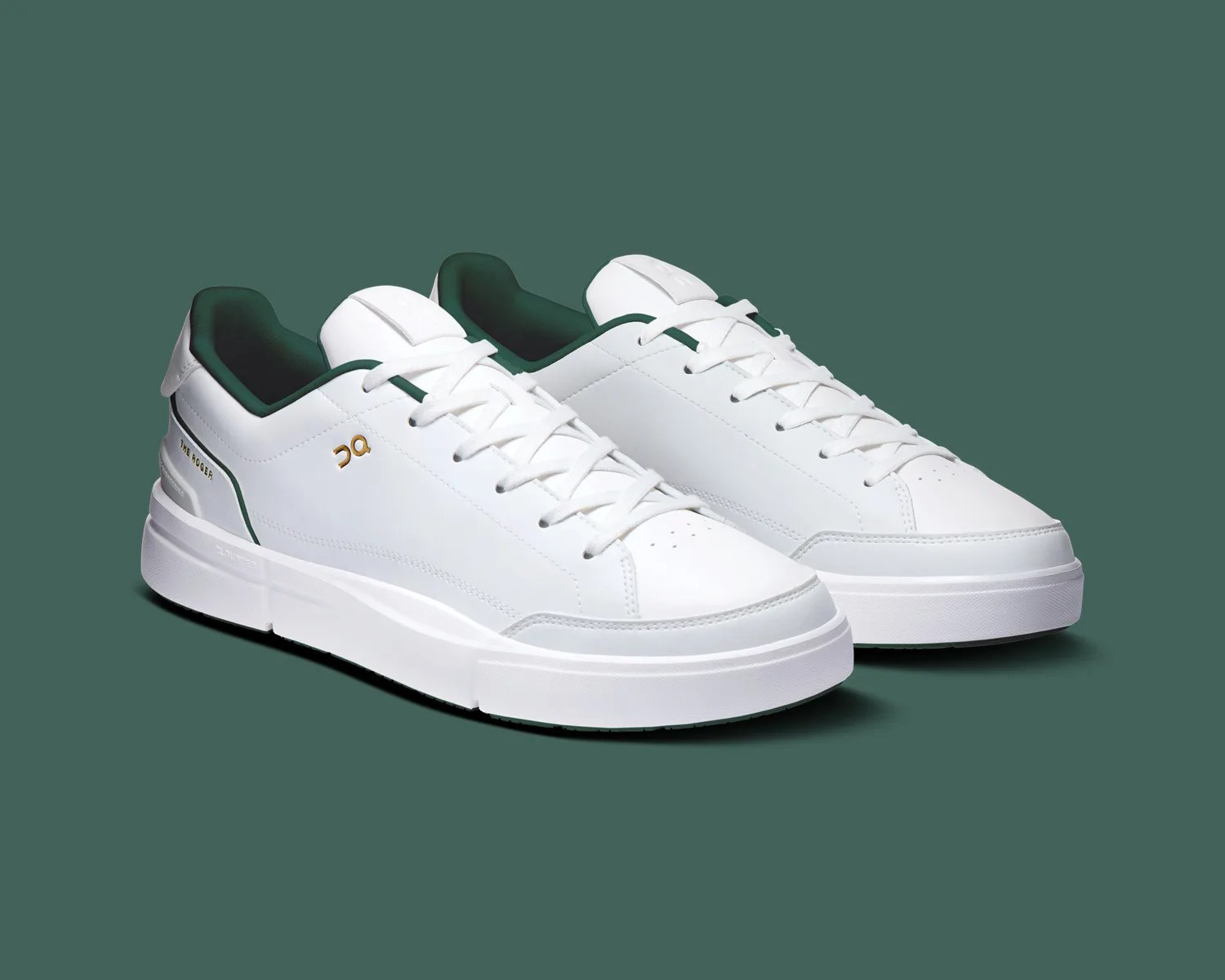 Pair of white low-top sneakers with dark green inner lining and gold logo on the side.