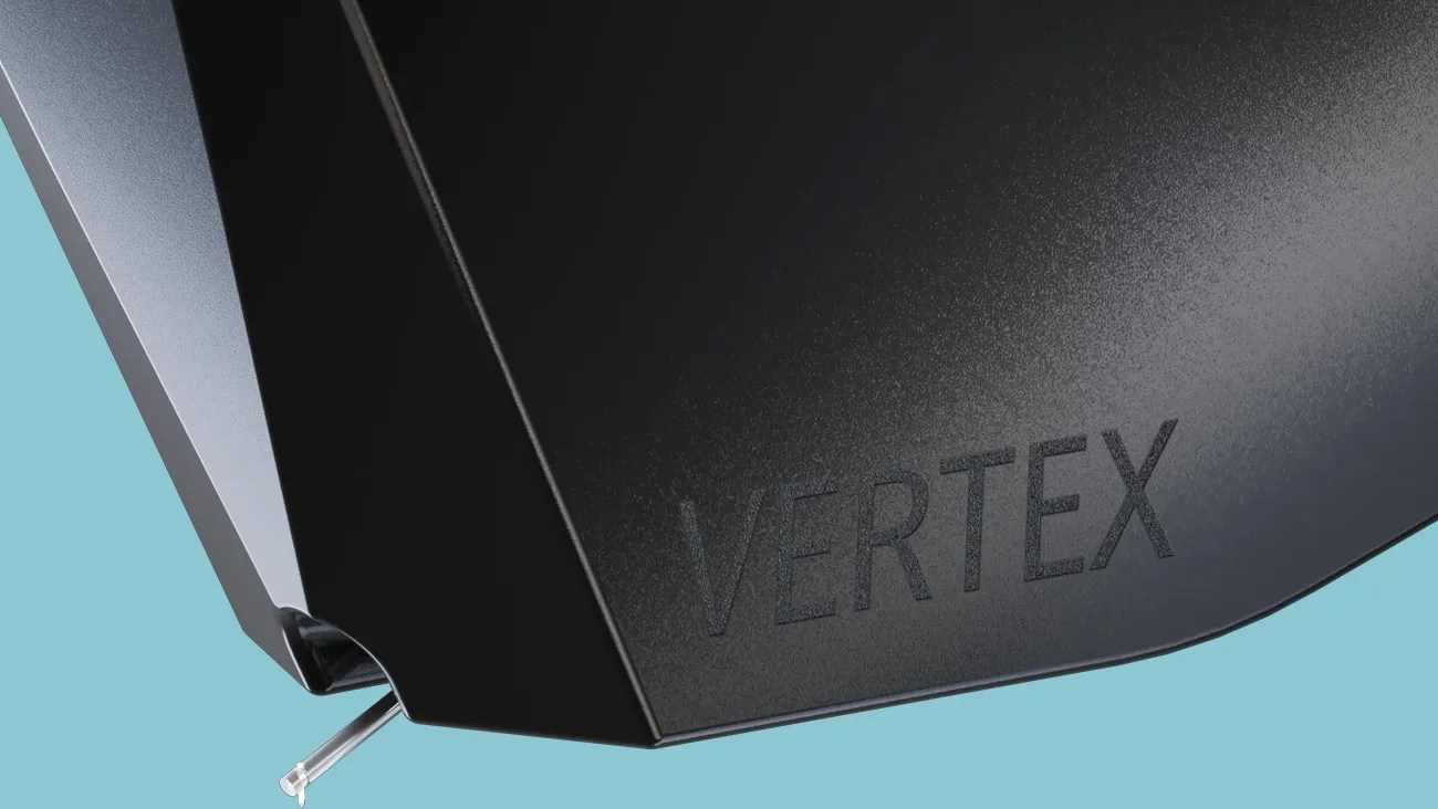 Close-up of a black textured surface with the word "VERTEX" embossed and a small transparent plastic peg attached.
