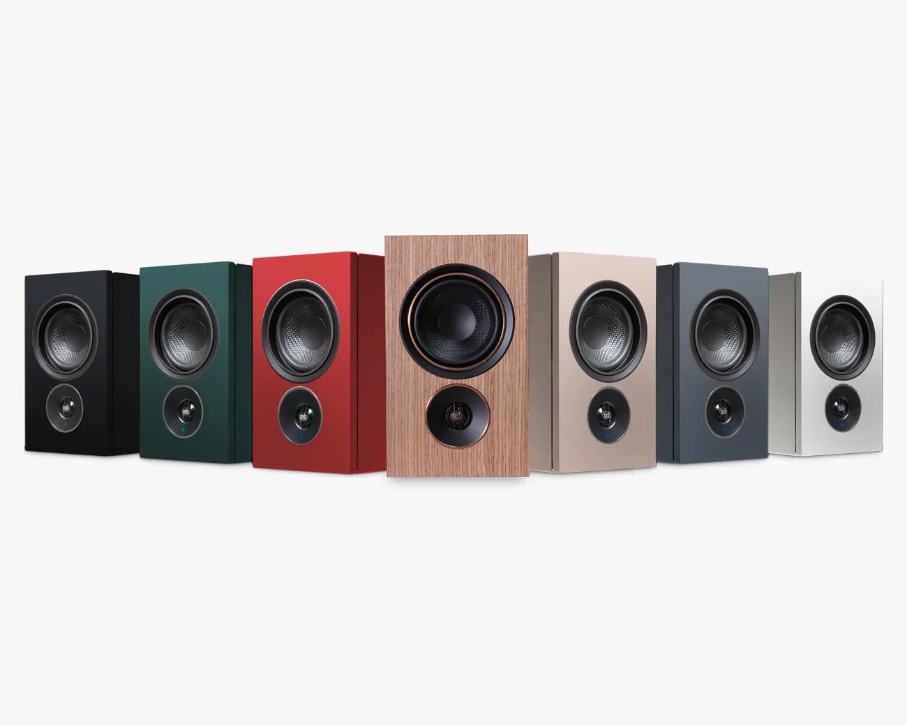 Seven bookshelf speakers in black, dark green, red, wood grain, beige, dark gray, and white colors arranged in a row.