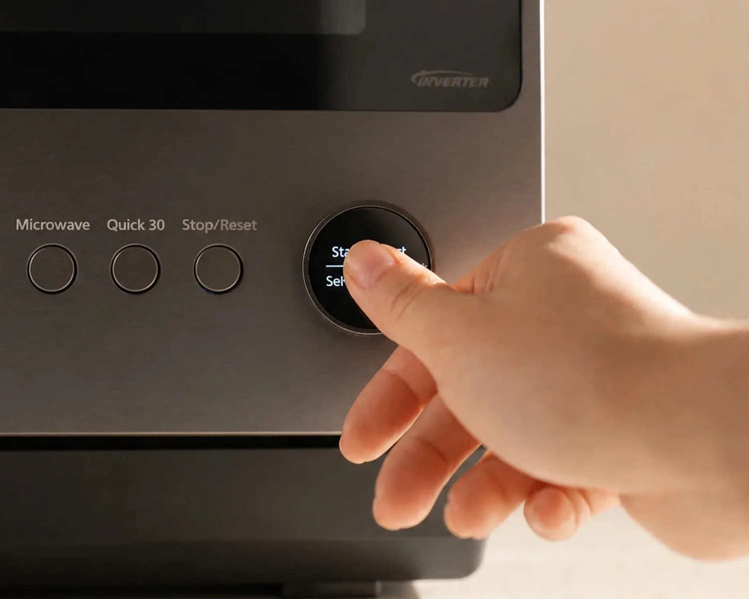 Hand adjusting the round control knob on a stainless steel microwave oven panel.
