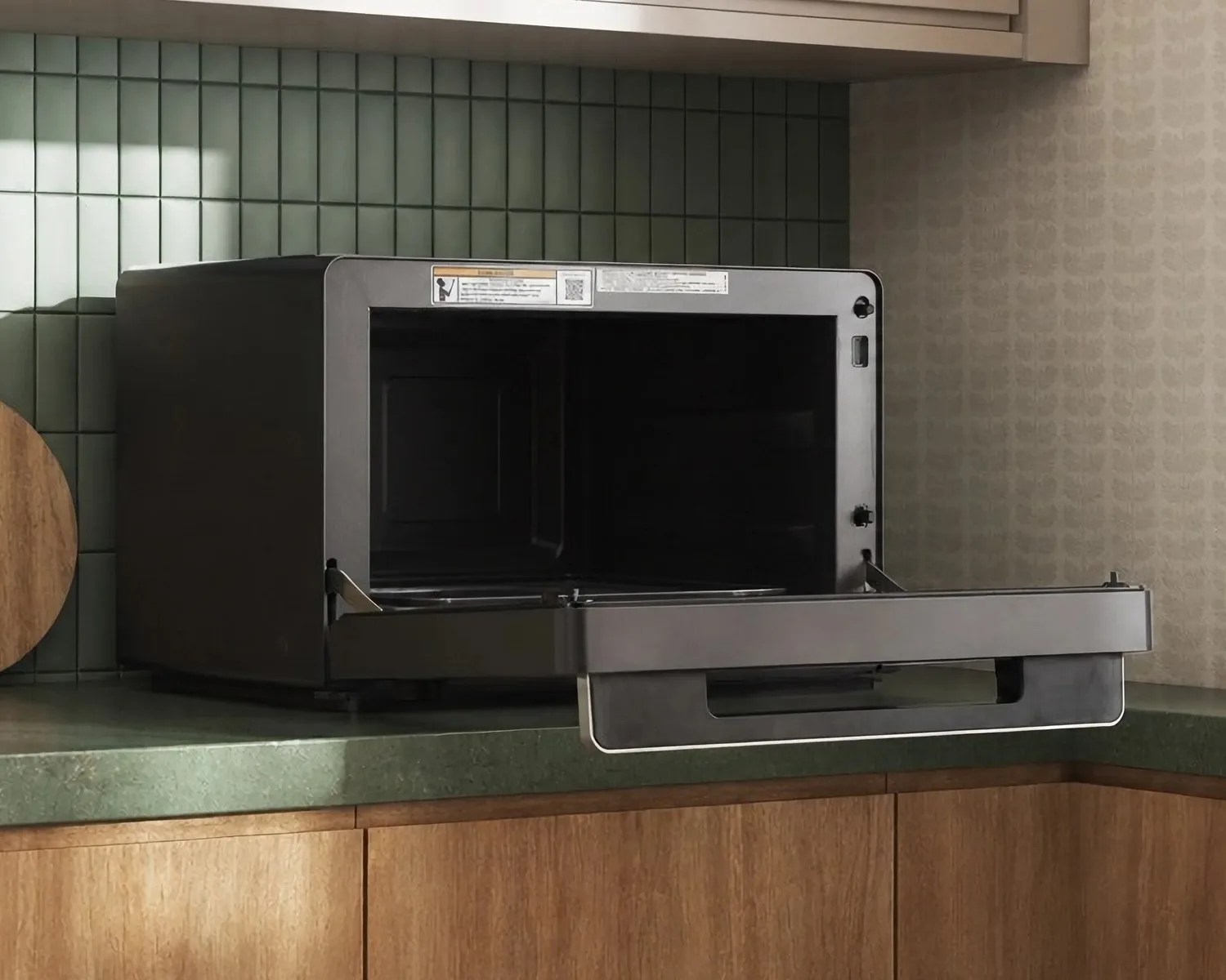 Black microwave oven with open door on green countertop in kitchen corner.