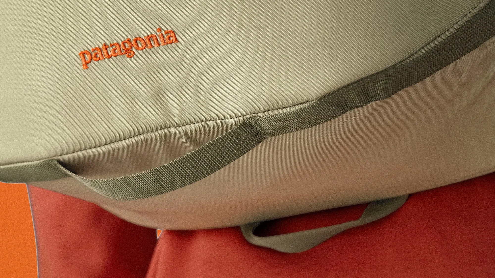 Close-up of a beige Patagonia bag with orange logo and green strap against an orange background.