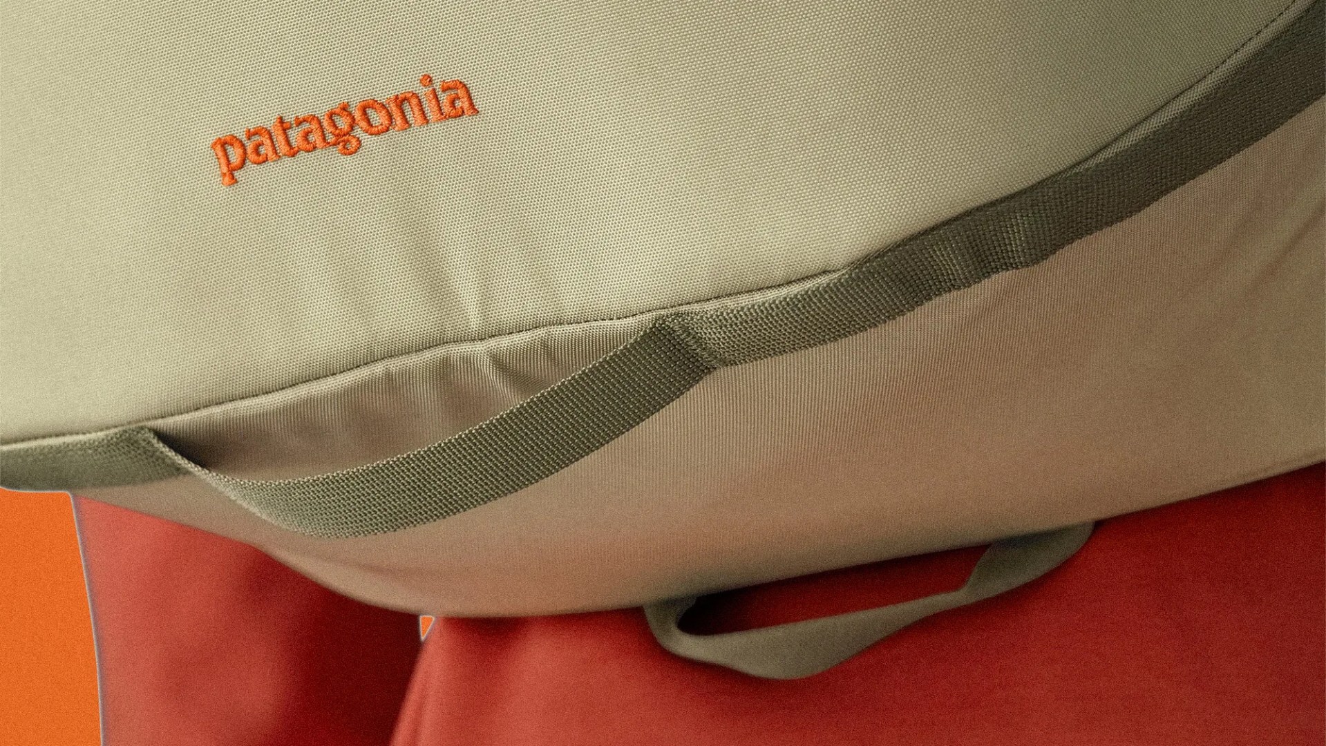 Close-up of a beige Patagonia bag with orange logo and green strap against an orange background.